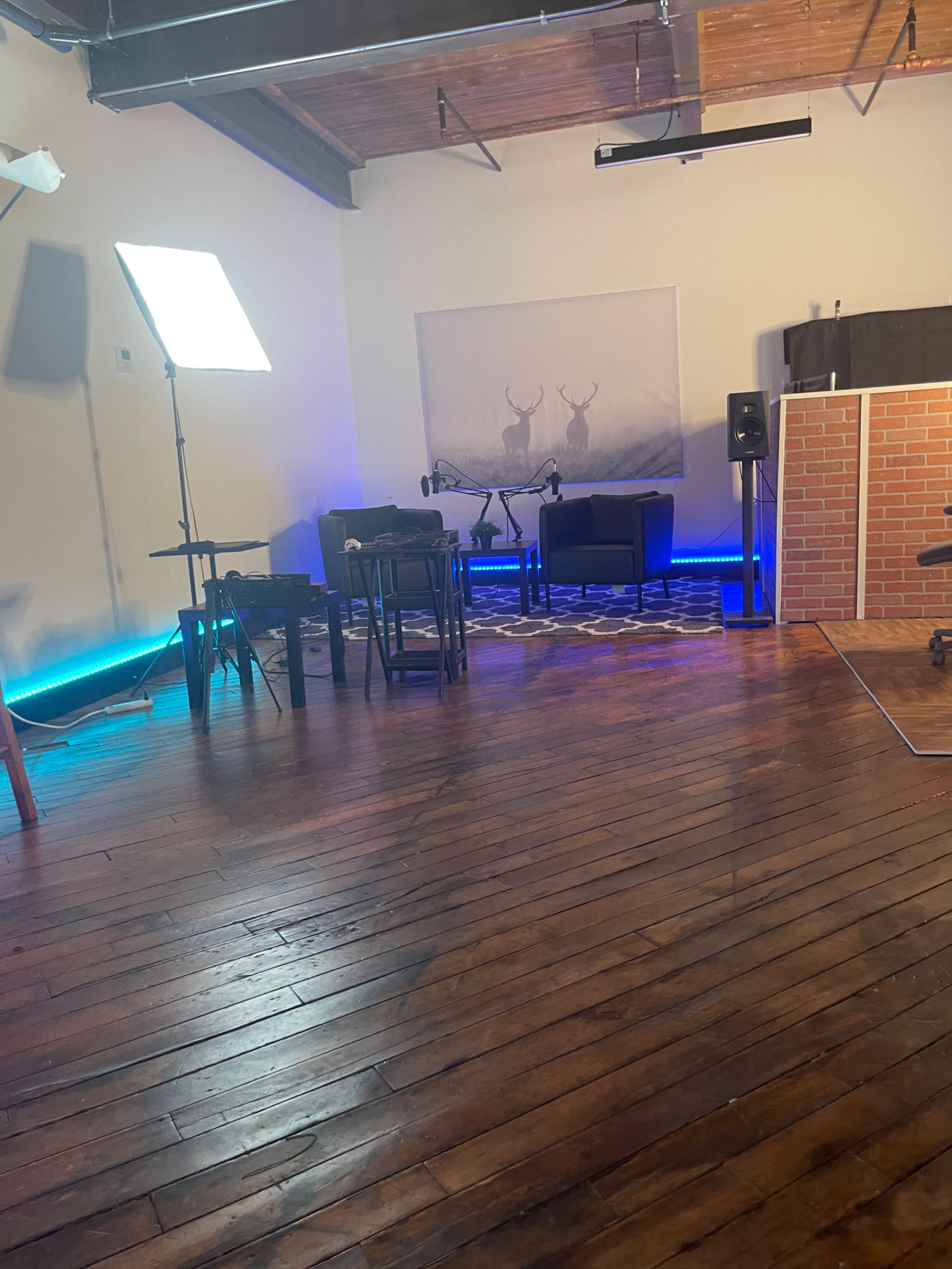 A spacious indoor setting with wooden floors, featuring a seating area with dark furniture, an illuminated backdrop, and a sound system in the corner.