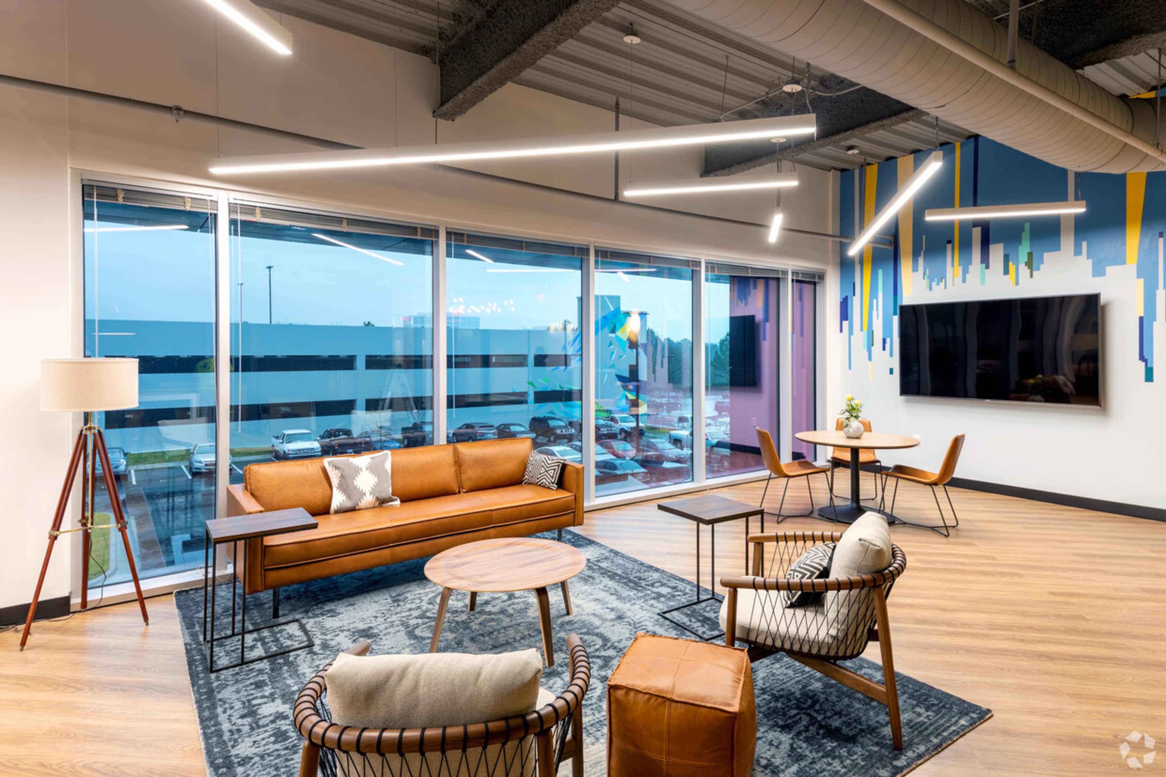 A modern lounge area featuring a brown leather couch, stylish armchairs, a coffee table, and large windows with a view of an outdoor space.