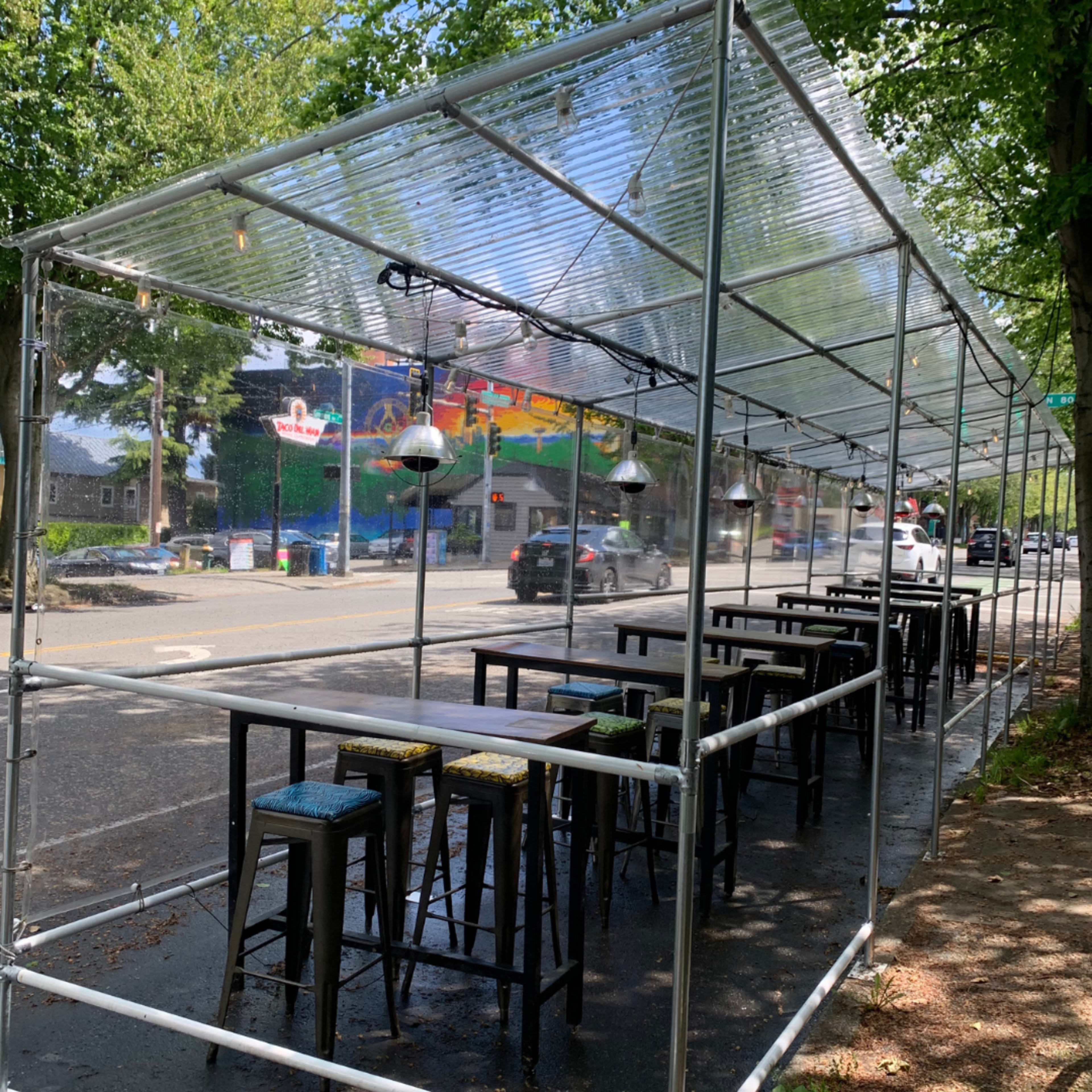 A covered outdoor dining area with high tables and stools set up beside a road.
