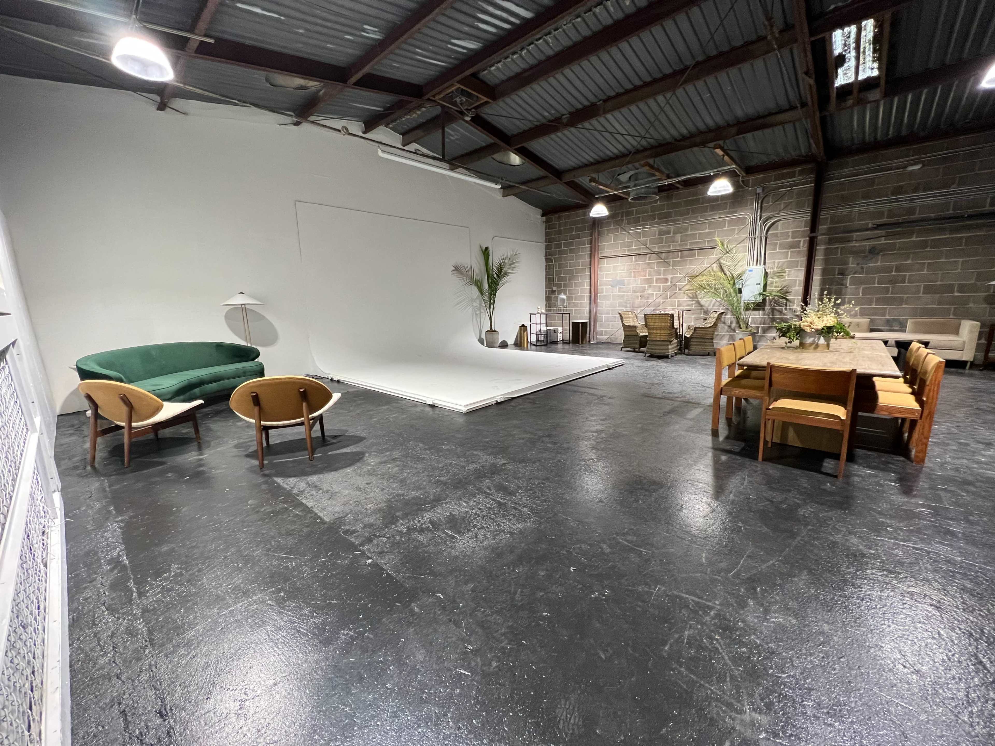An industrial-style interior space featuring a green sofa, two wooden chairs, a dining table, and a backdrop area.
