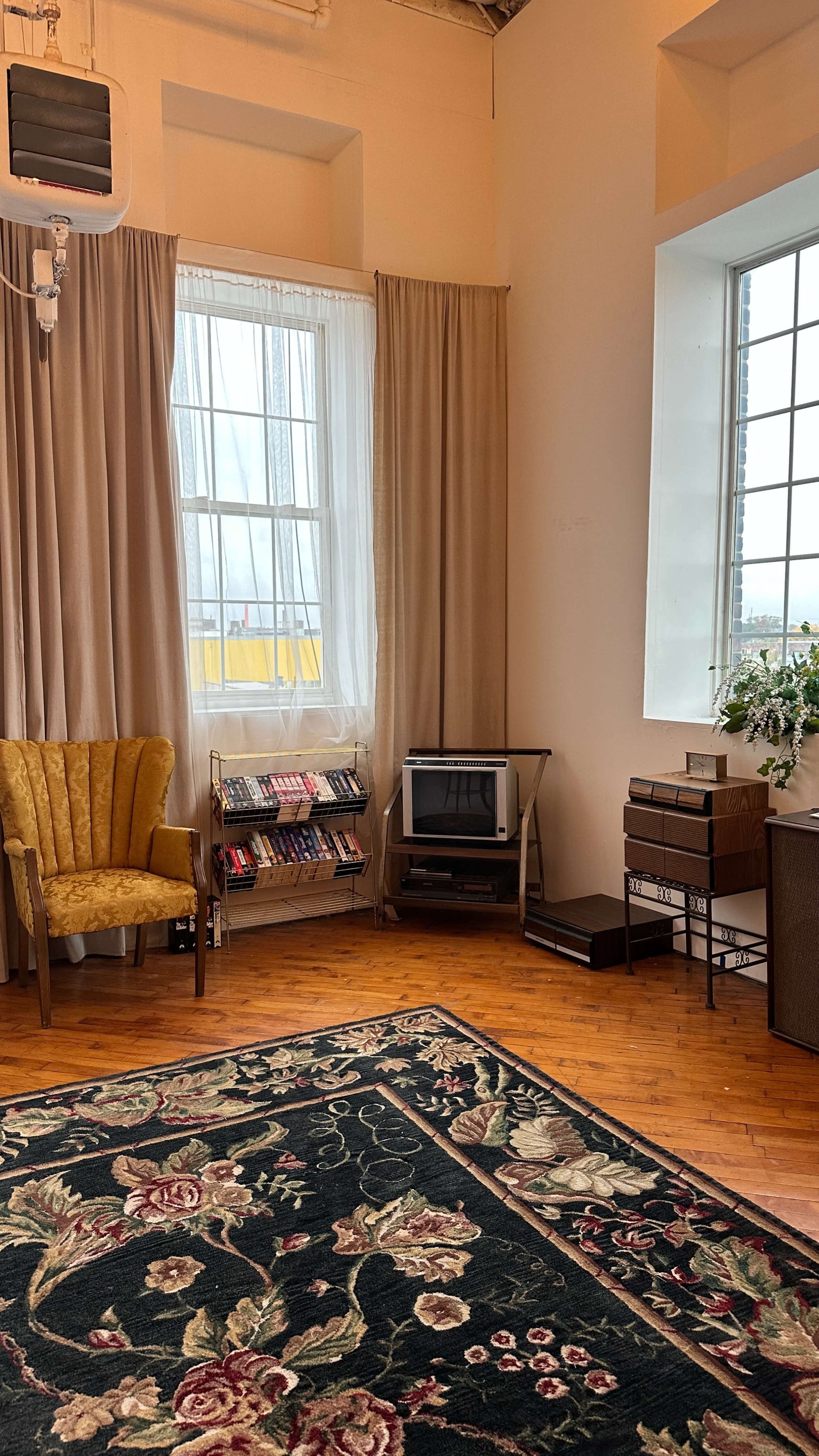 The room features a yellow armchair, a bookshelf with books, a vintage television, and a dark floral carpet.