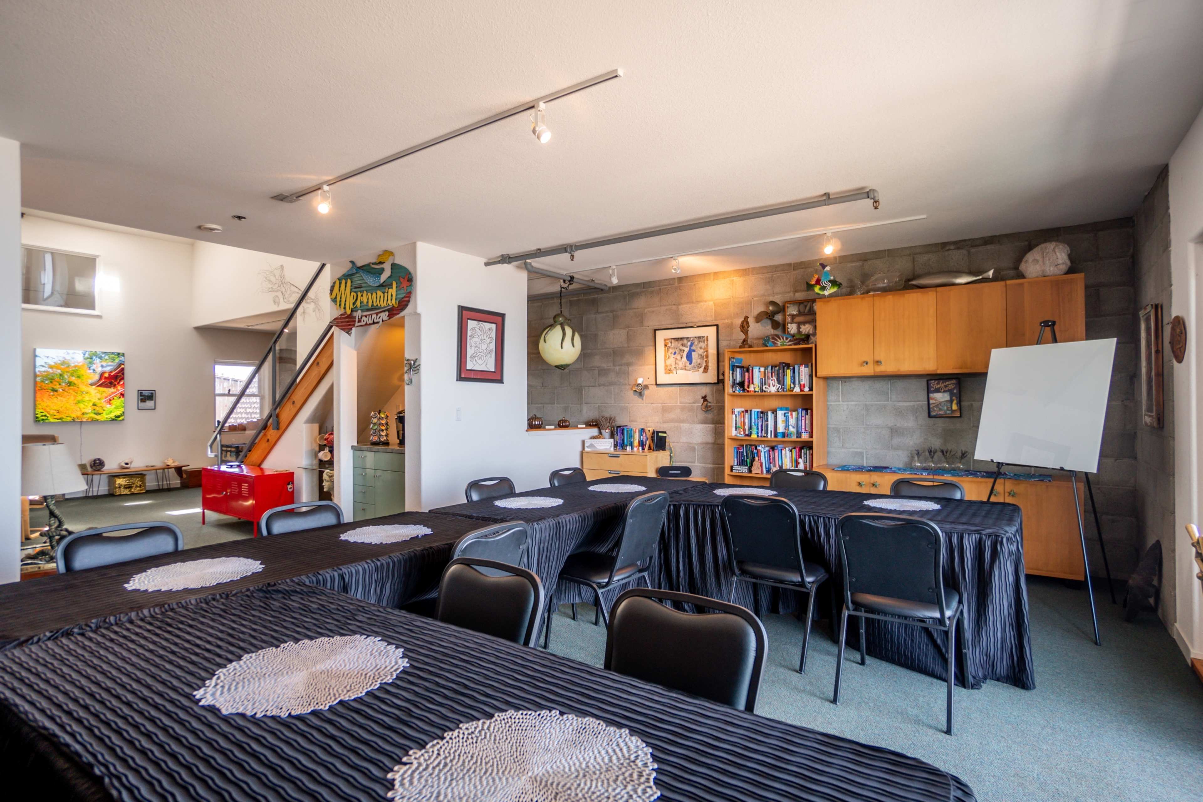 The image shows a conference room with black tables arranged in a U-shape, surrounded by black chairs, and a wooden cabinet filled with books in the background.