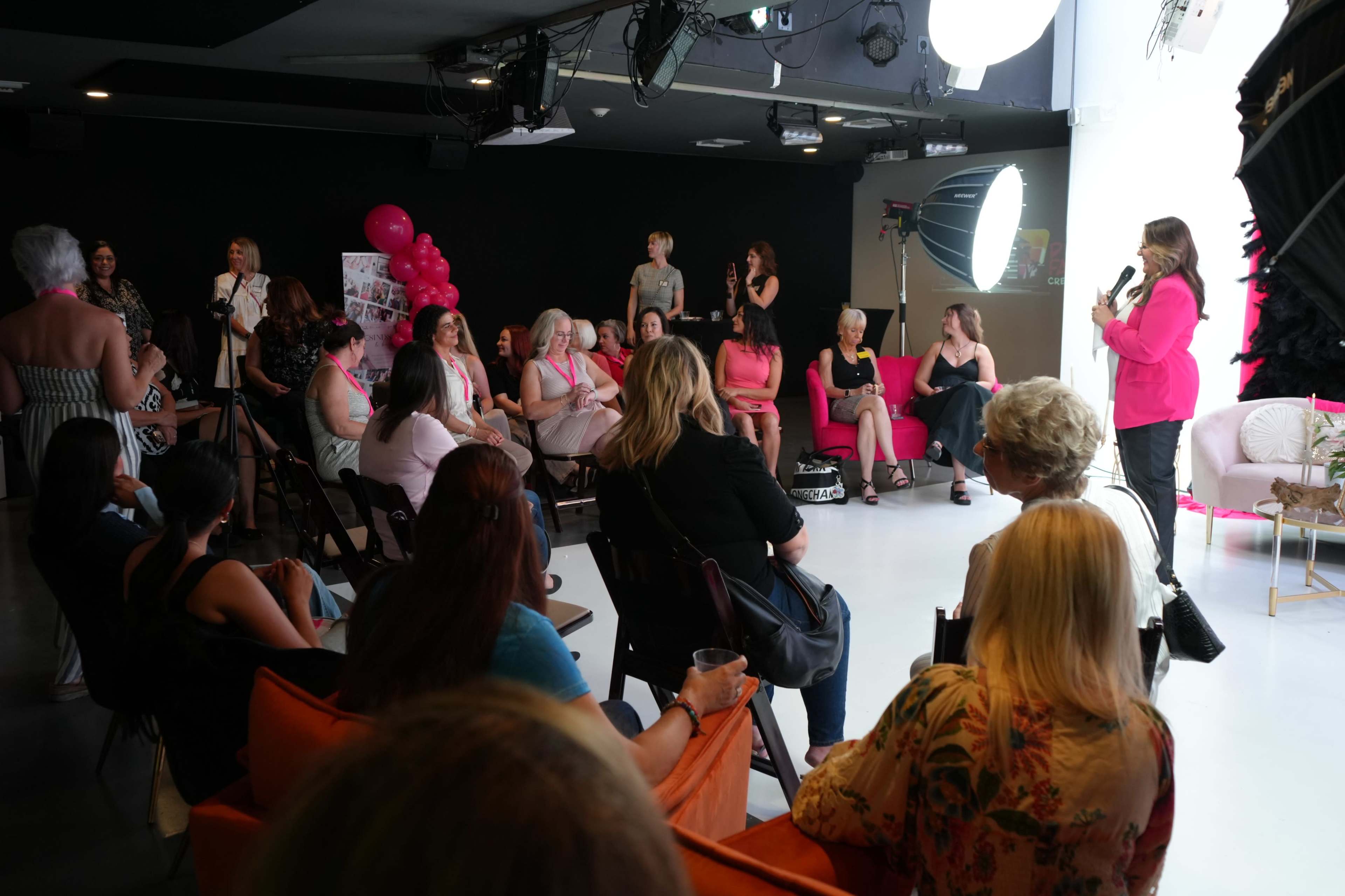 A group of women is seated in a studio setting, engaged in a discussion while a speaker addresses them from the front.