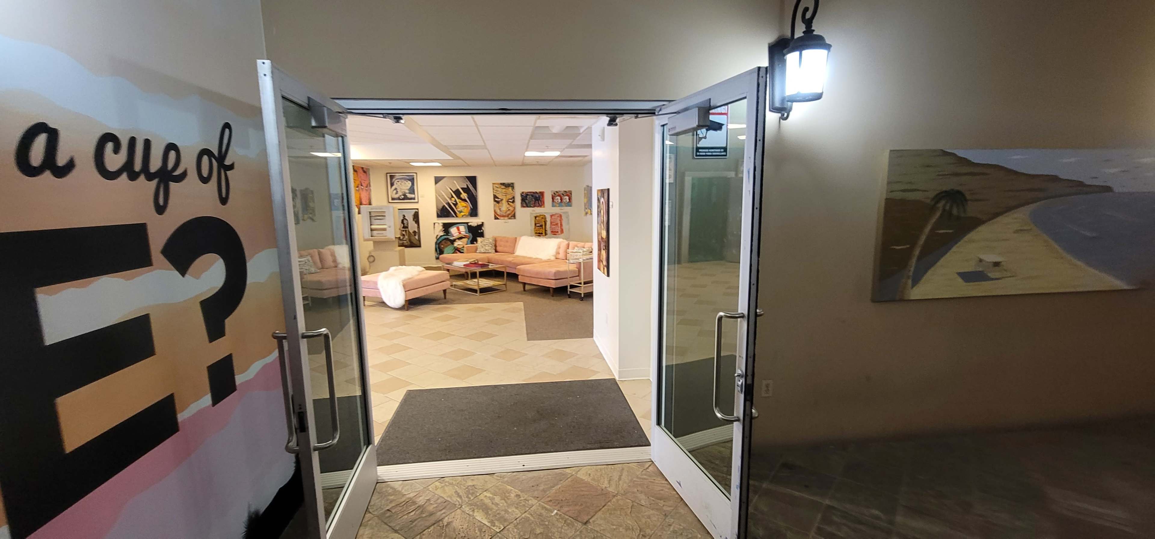 An open doorway leading into a brightly lit lounge area with pink seating and various artworks on the walls.
