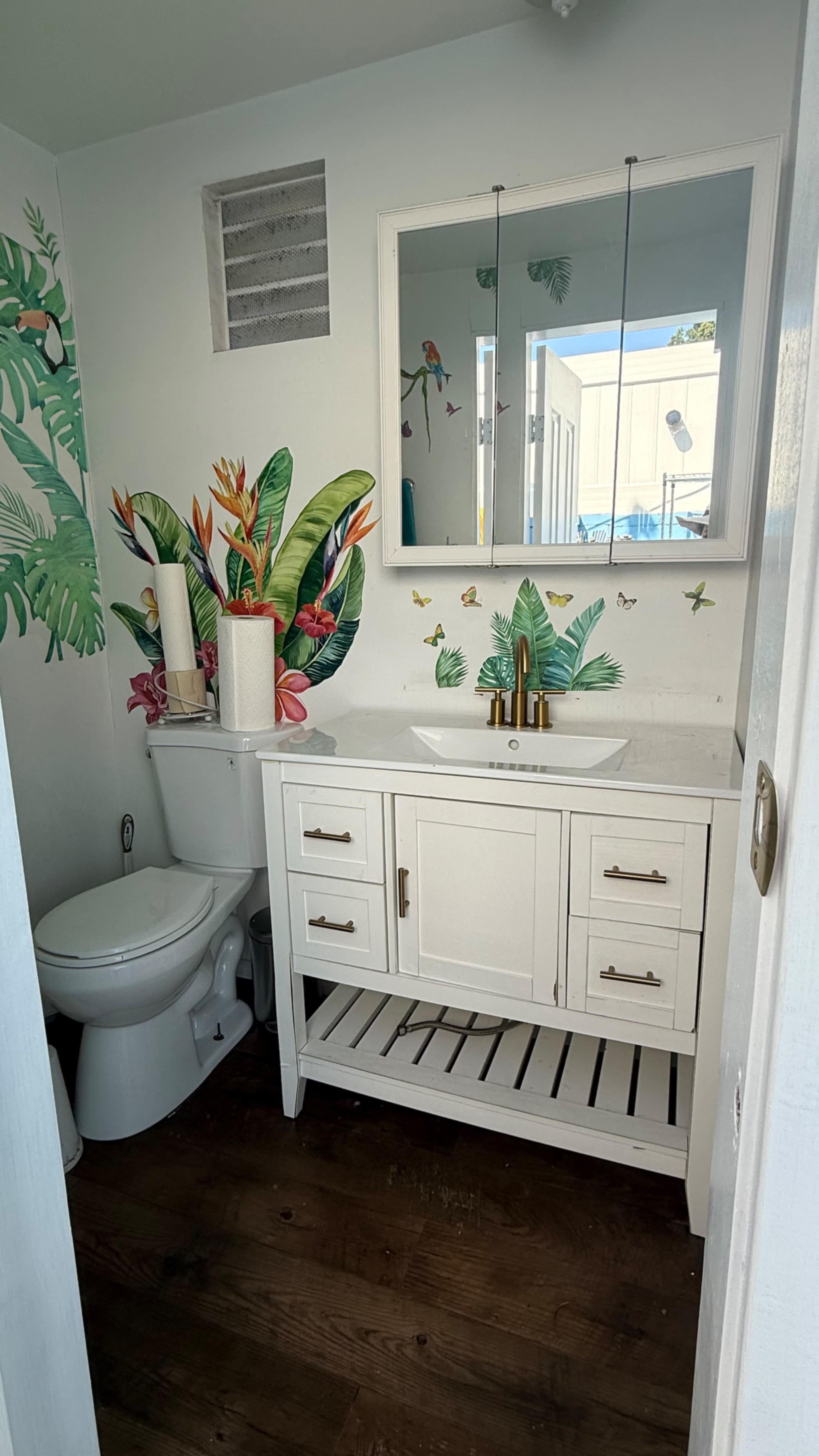 The bathroom features a white vanity with a sink, a toilet, and walls adorned with vibrant plant and butterfly designs.