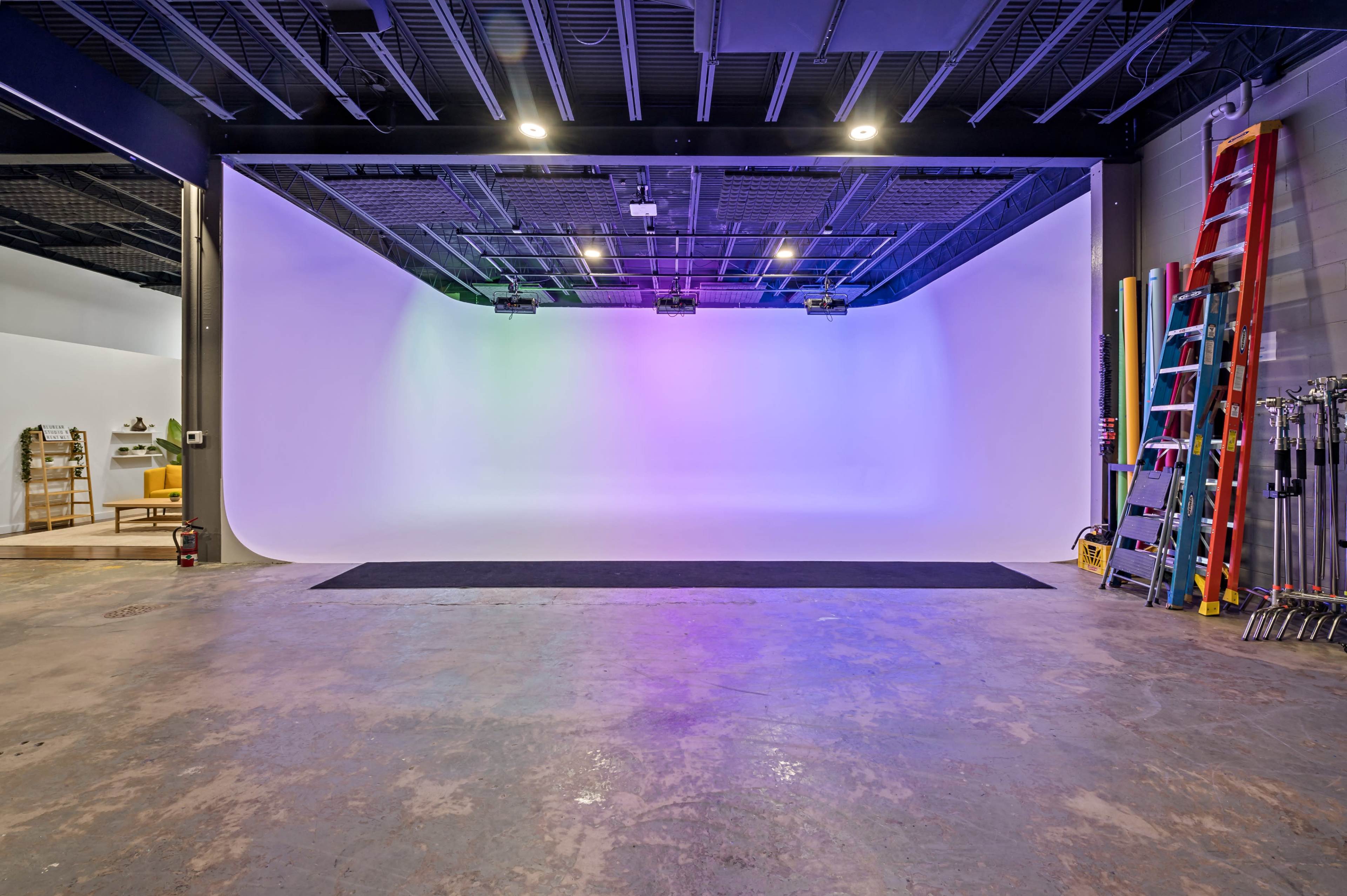An empty photo studio with a curved backdrop, colorful lighting, and various equipment visible in the background.