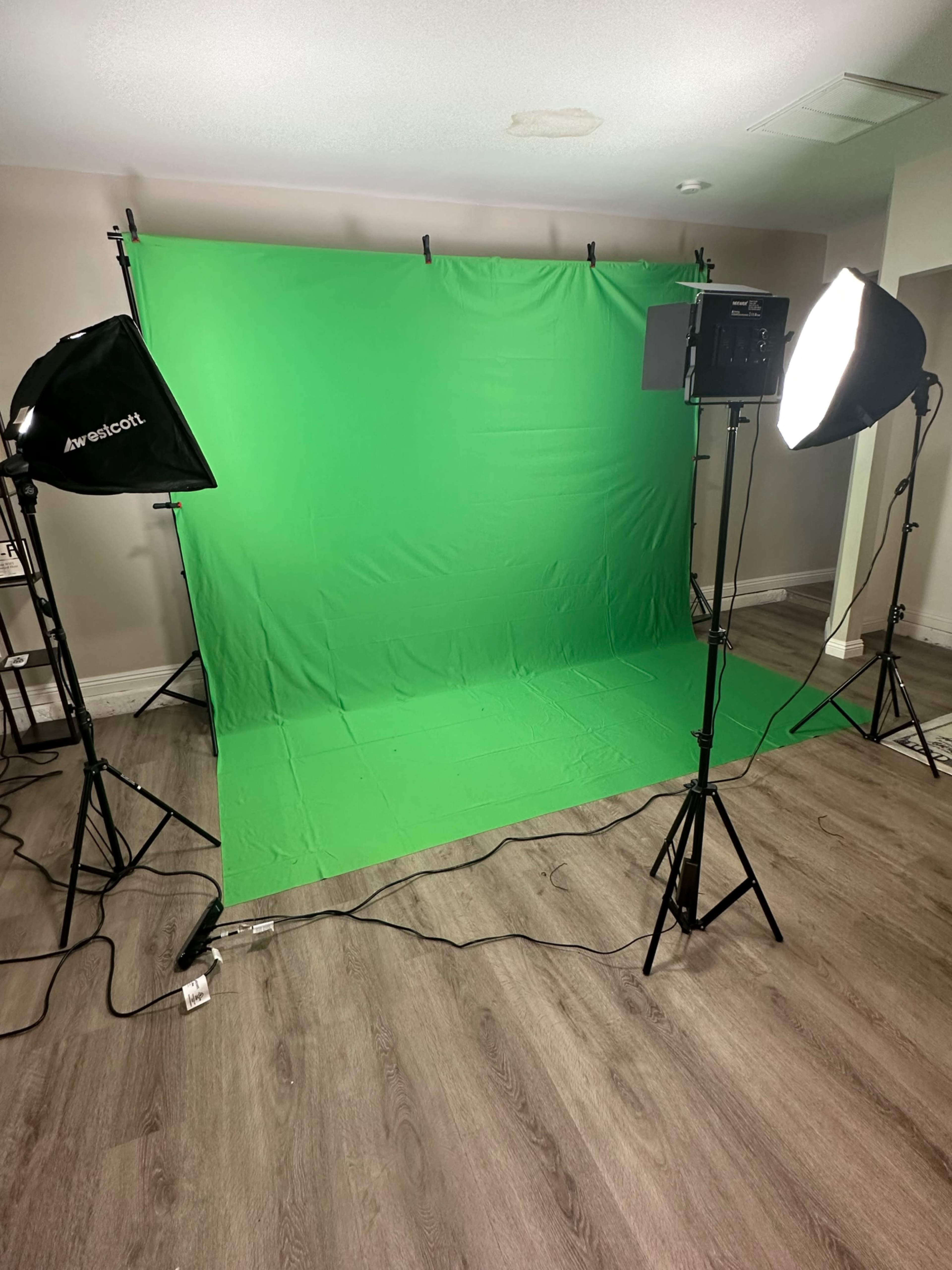 A studio setup with a green screen backdrop, two softbox lights, and a wooden floor.