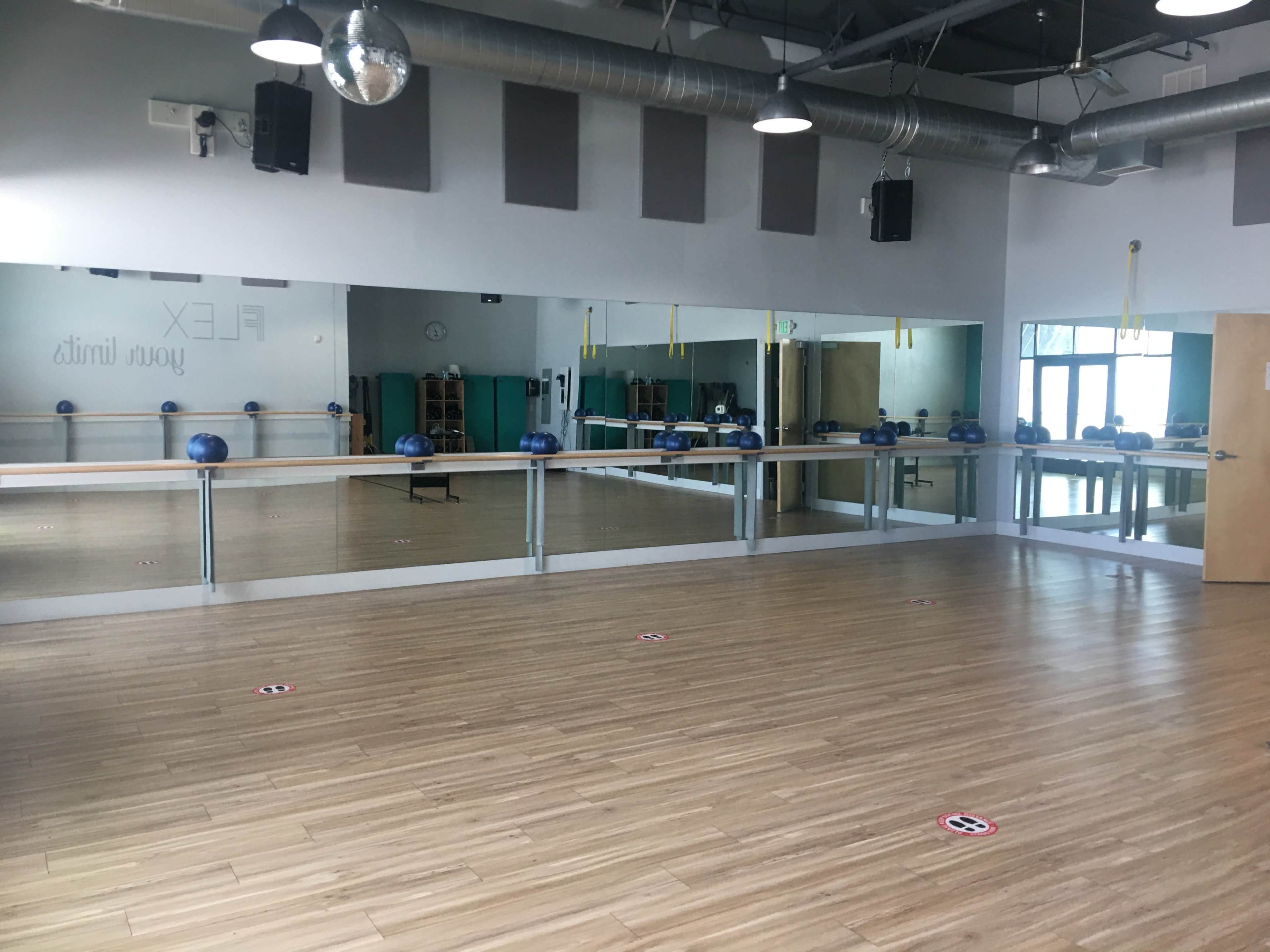 A spacious fitness studio with a wooden floor, large mirrors, and equipment placed along the walls.