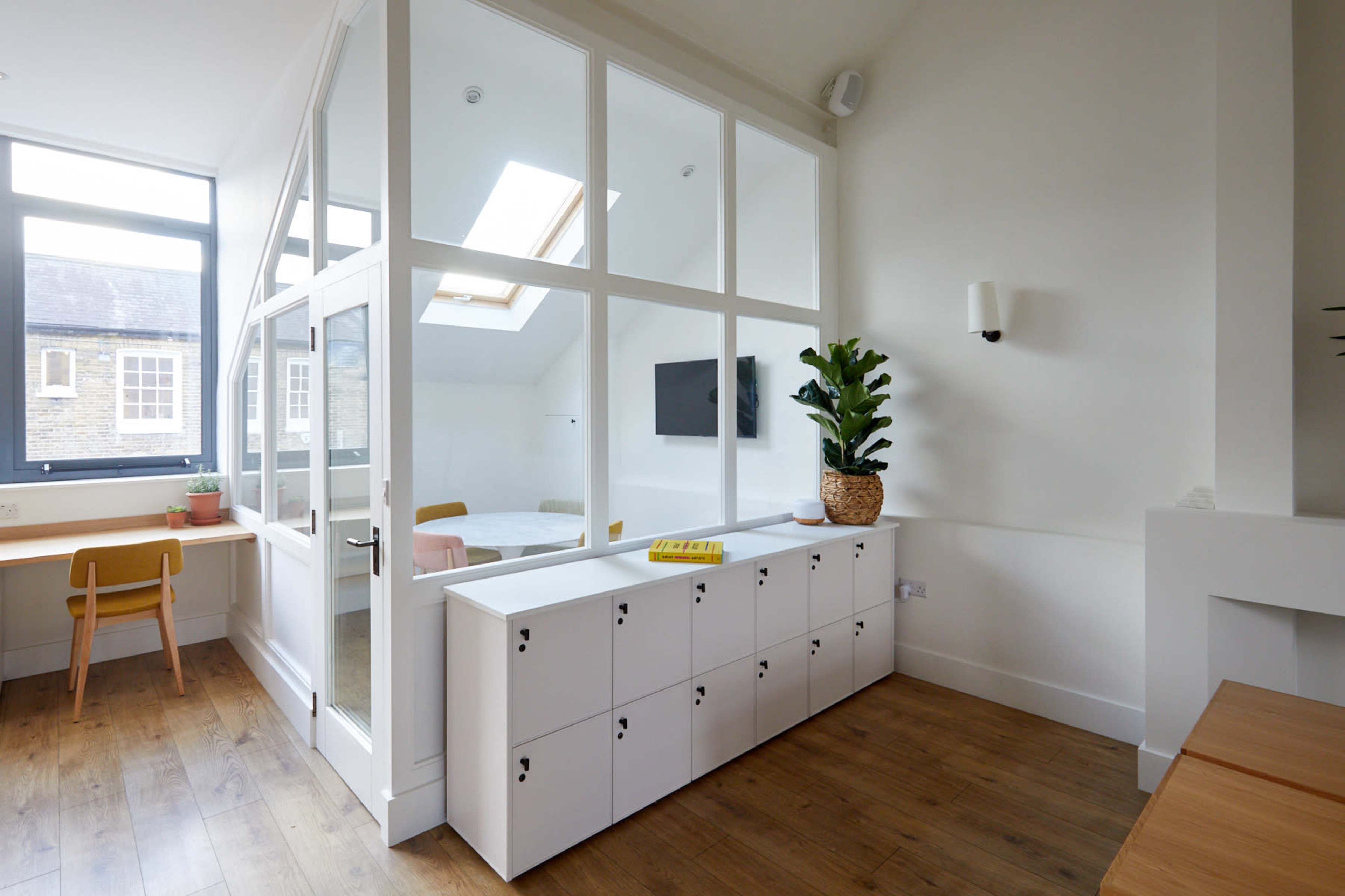 A modern interior with a glass-enclosed room, wooden flooring, and a white storage unit featuring multiple compartments.