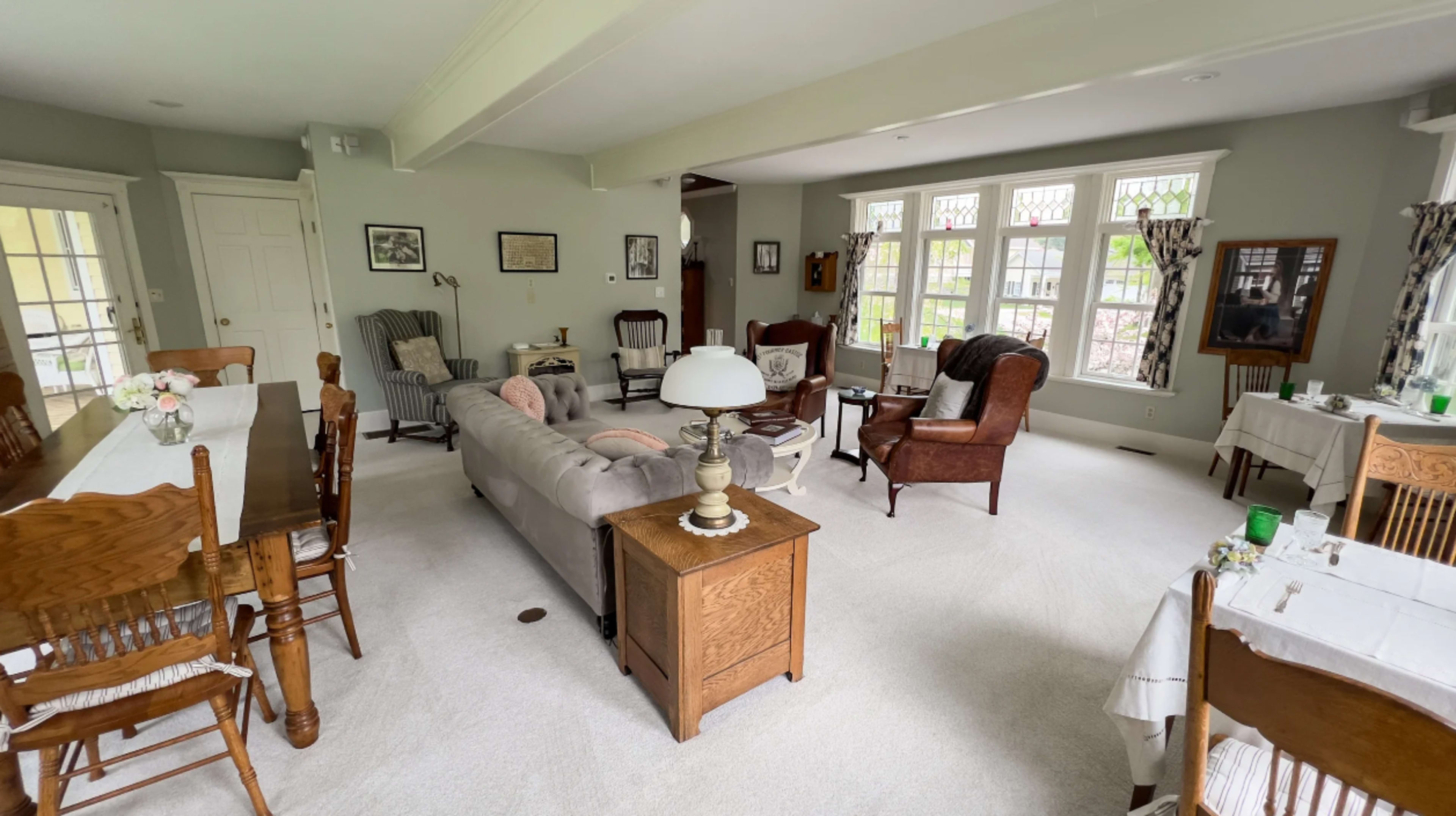 The room features a living area with a mix of brown leather and fabric seating arranged around a coffee table, a dining table with wooden chairs, and large windows letting in natural light.