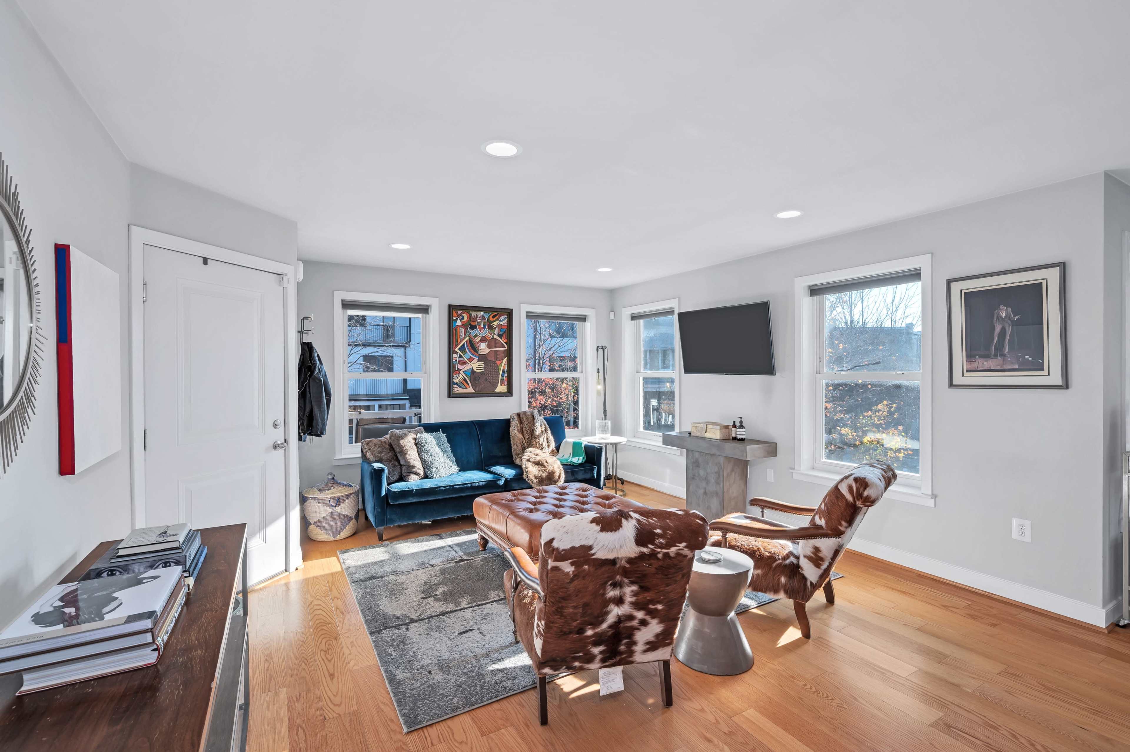 The room features a cozy seating area with a blue sofa, two armchairs, and large windows allowing natural light to enter.