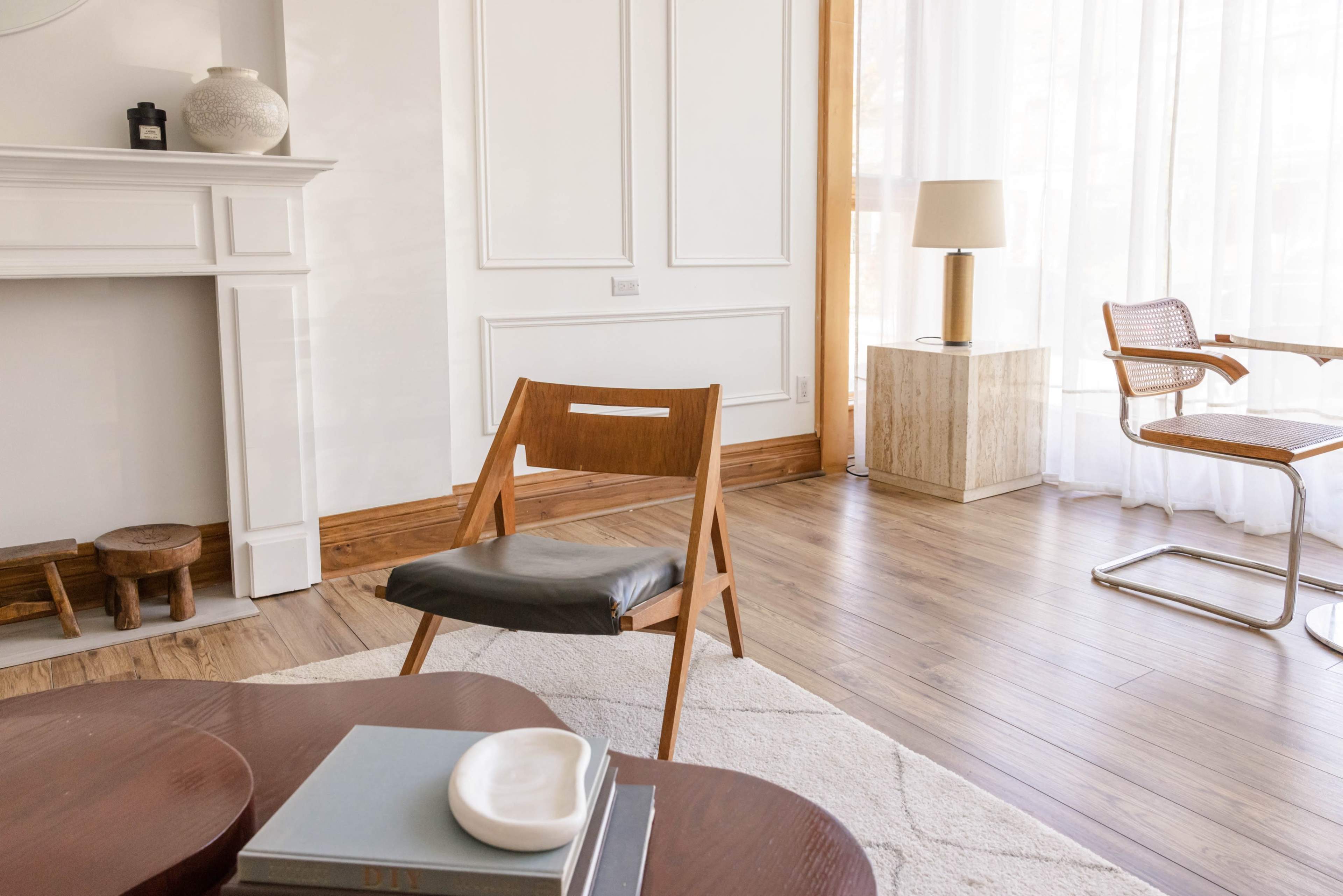 A wooden chair and a small round table are positioned in a well-lit room with hardwood floors and large windows.