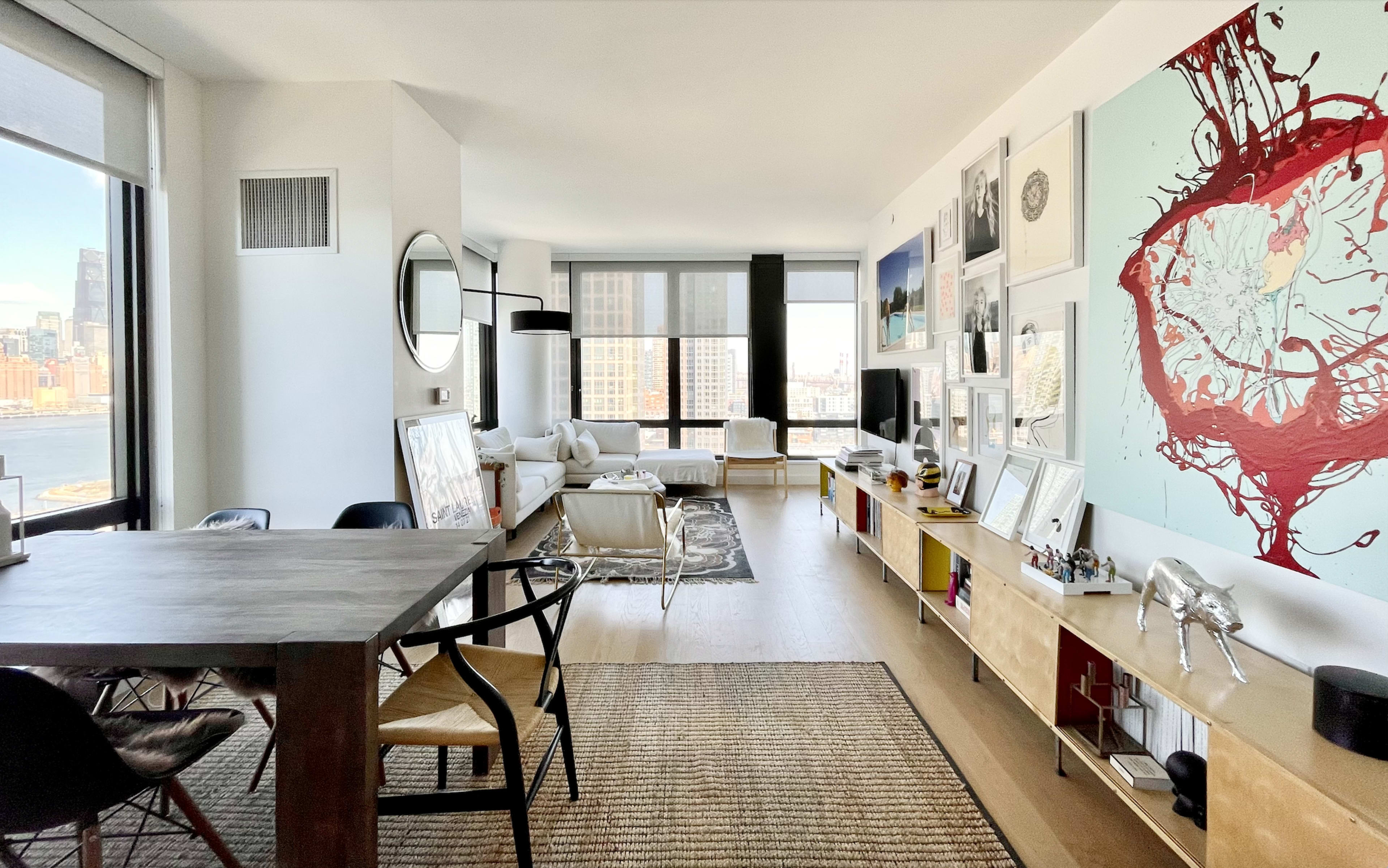 A bright, contemporary living space features a dining area with a large table, a cozy seating area, and a wall adorned with abstract artwork.