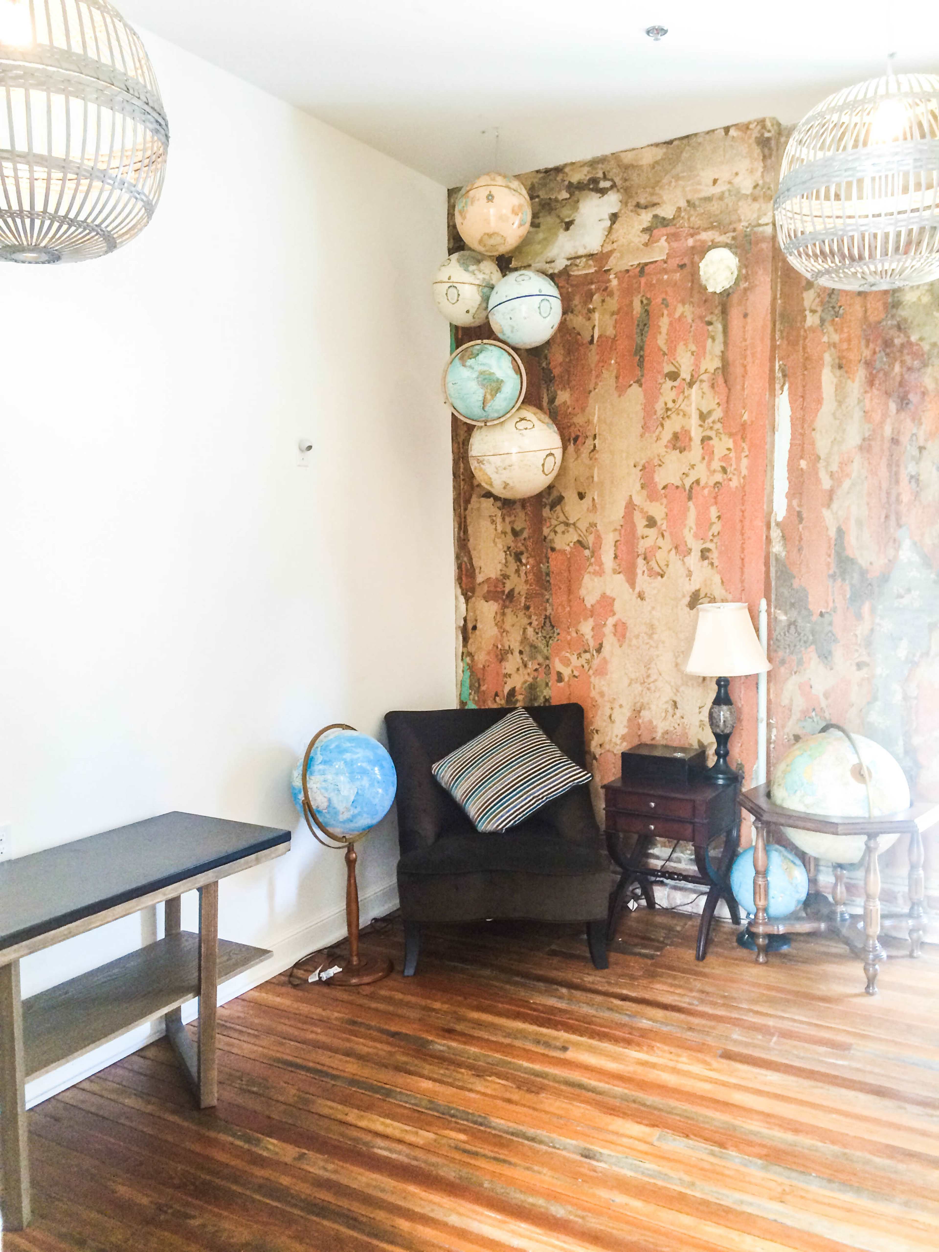 A room with a worn, rustic wall and several globes placed near a brown chair and a small table.
