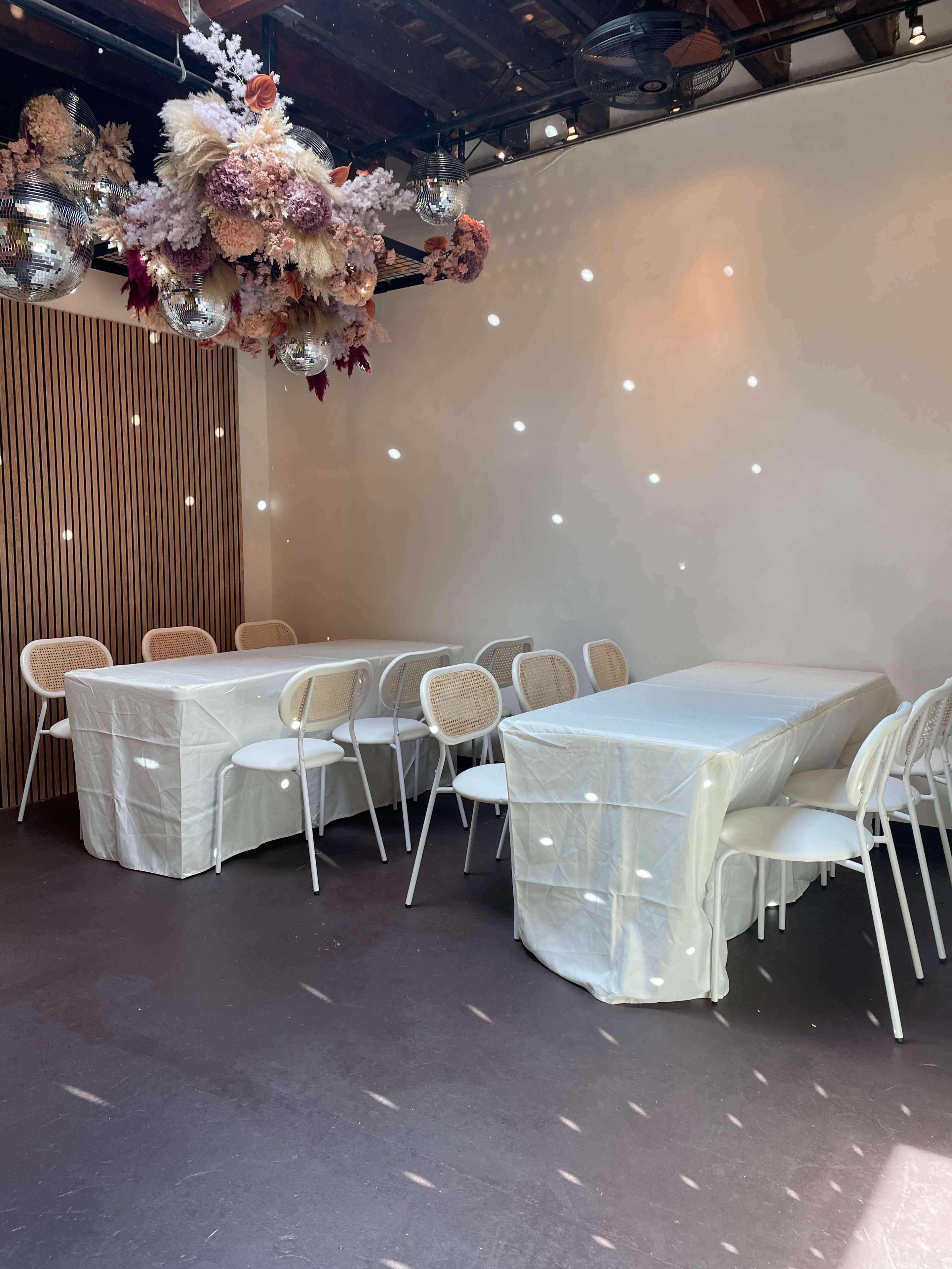A softly lit room with white tables covered in linen and decorated with hanging floral arrangements.