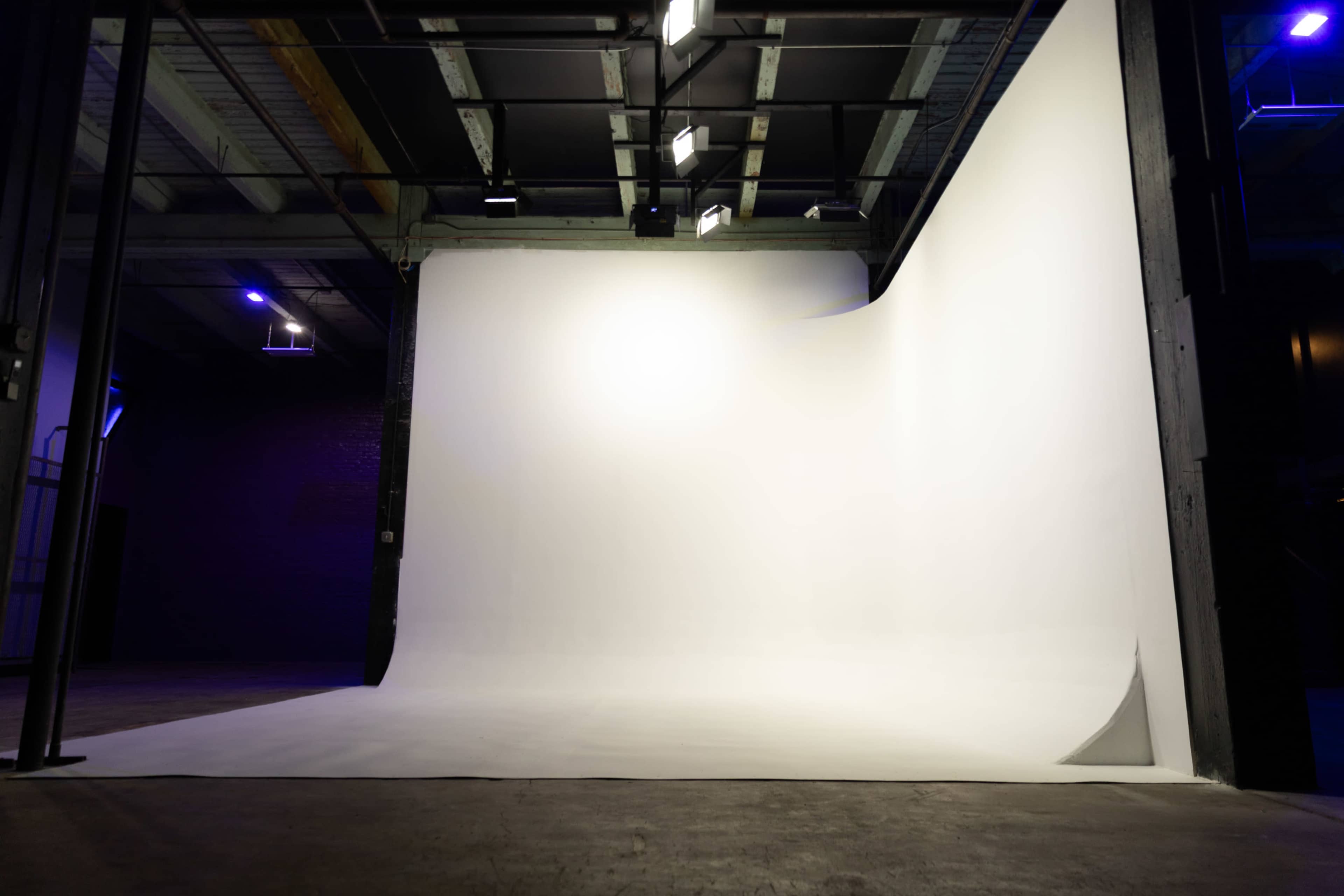 The image shows a spacious photography studio with a smooth, white backdrop and dim lighting.