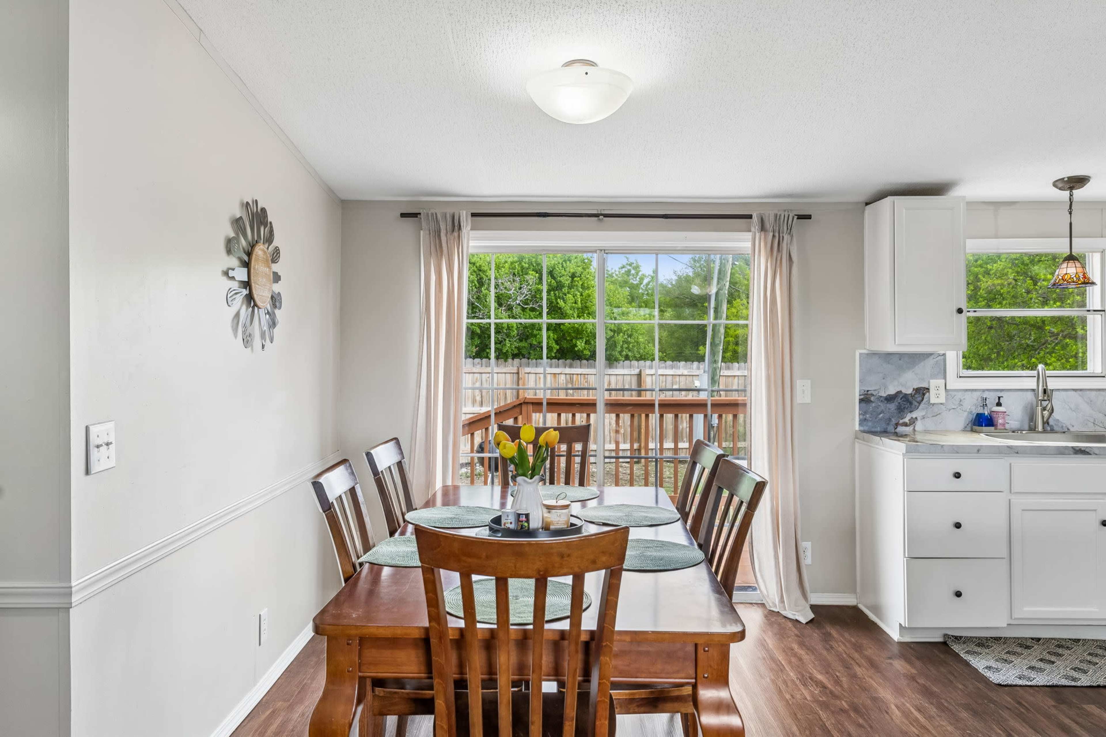 A dining area features a wooden table set for a meal, with a view of a backyard visible through a large window.