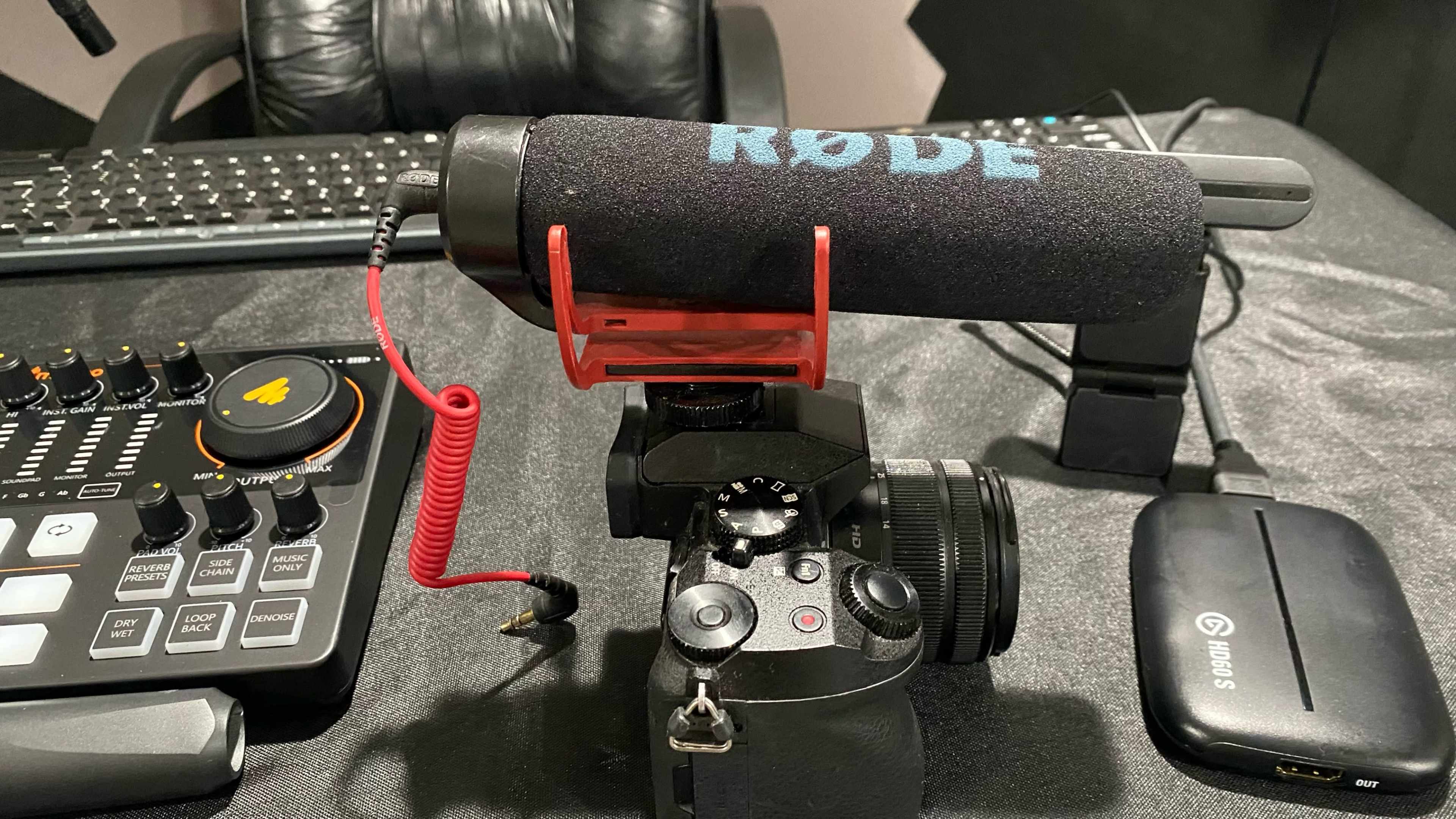 The image shows a camera with a Rode microphone attached to it, positioned on a desk alongside audio equipment and a keyboard.