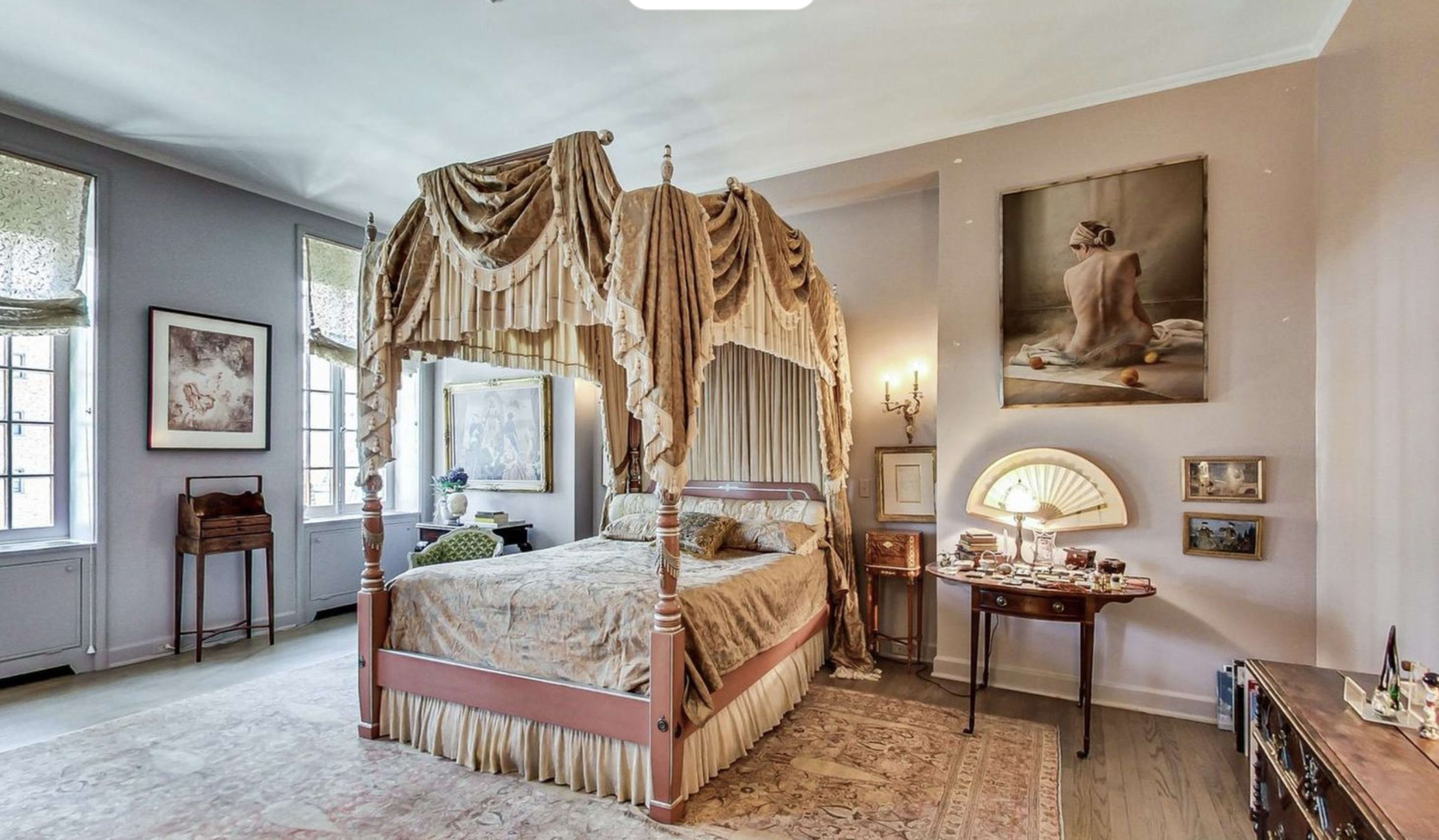 A bedroom featuring a canopy bed draped with fabric, a painting on the wall, and various furnishings arranged around the space.
