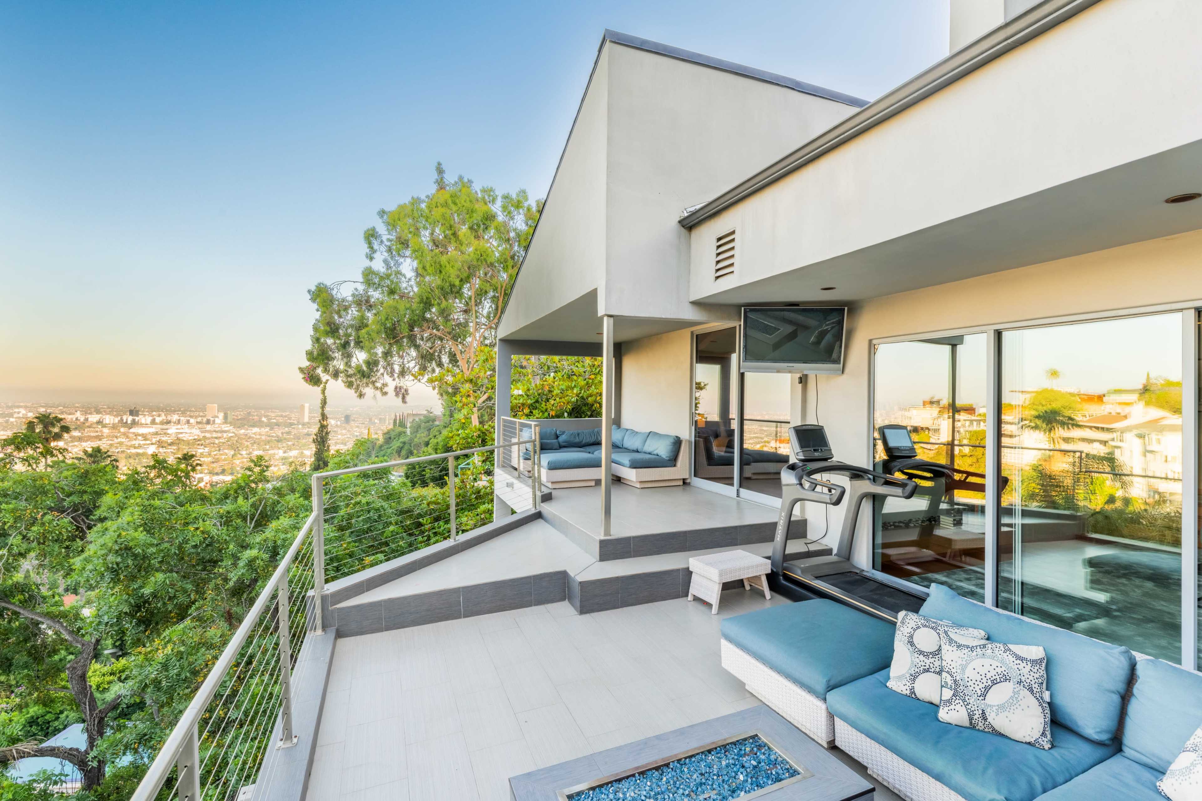 A modern patio with outdoor seating and a treadmill overlooks a cityscape.