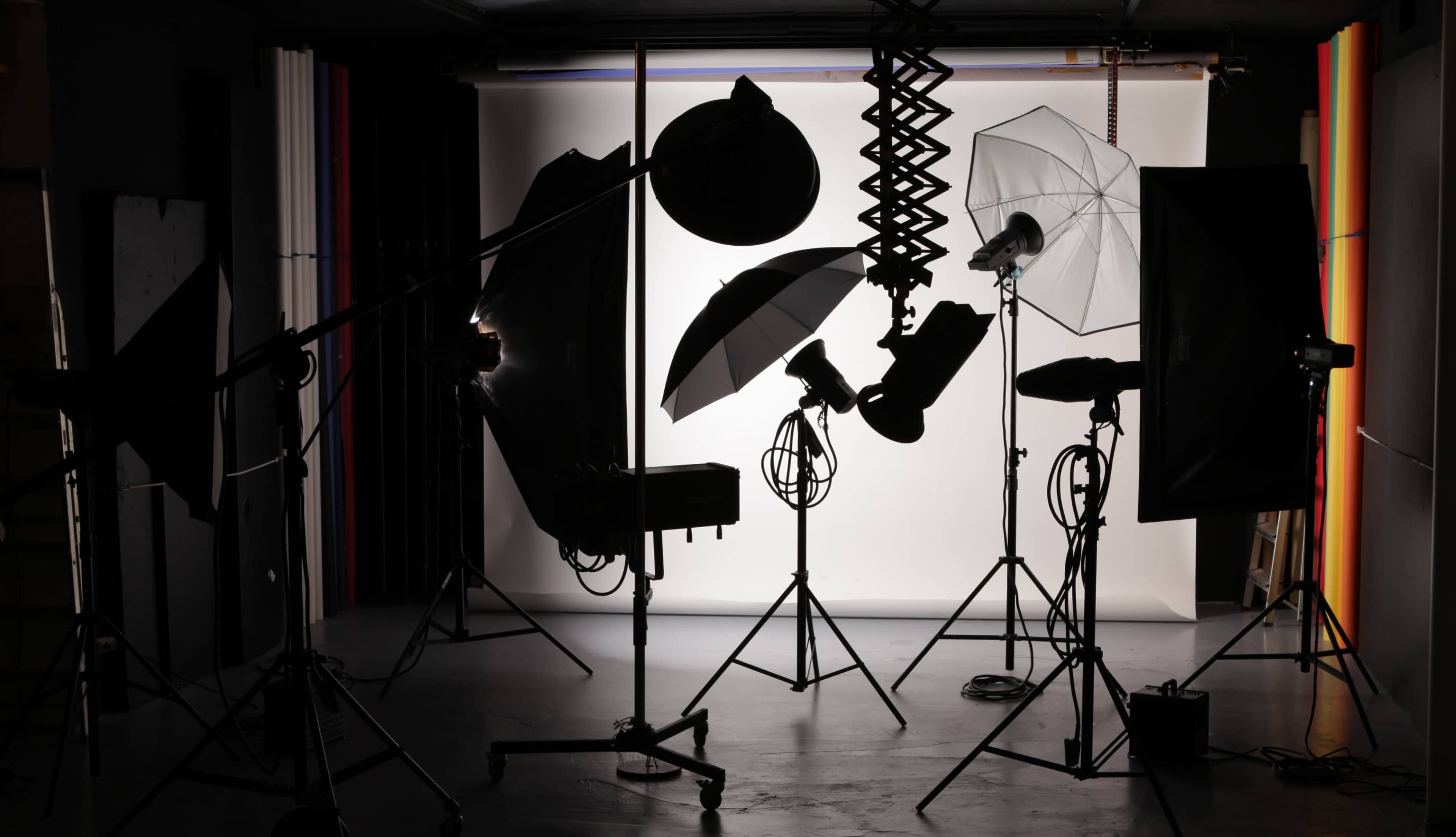 A photography studio setup with various lights and equipment silhouetted against a white backdrop.
