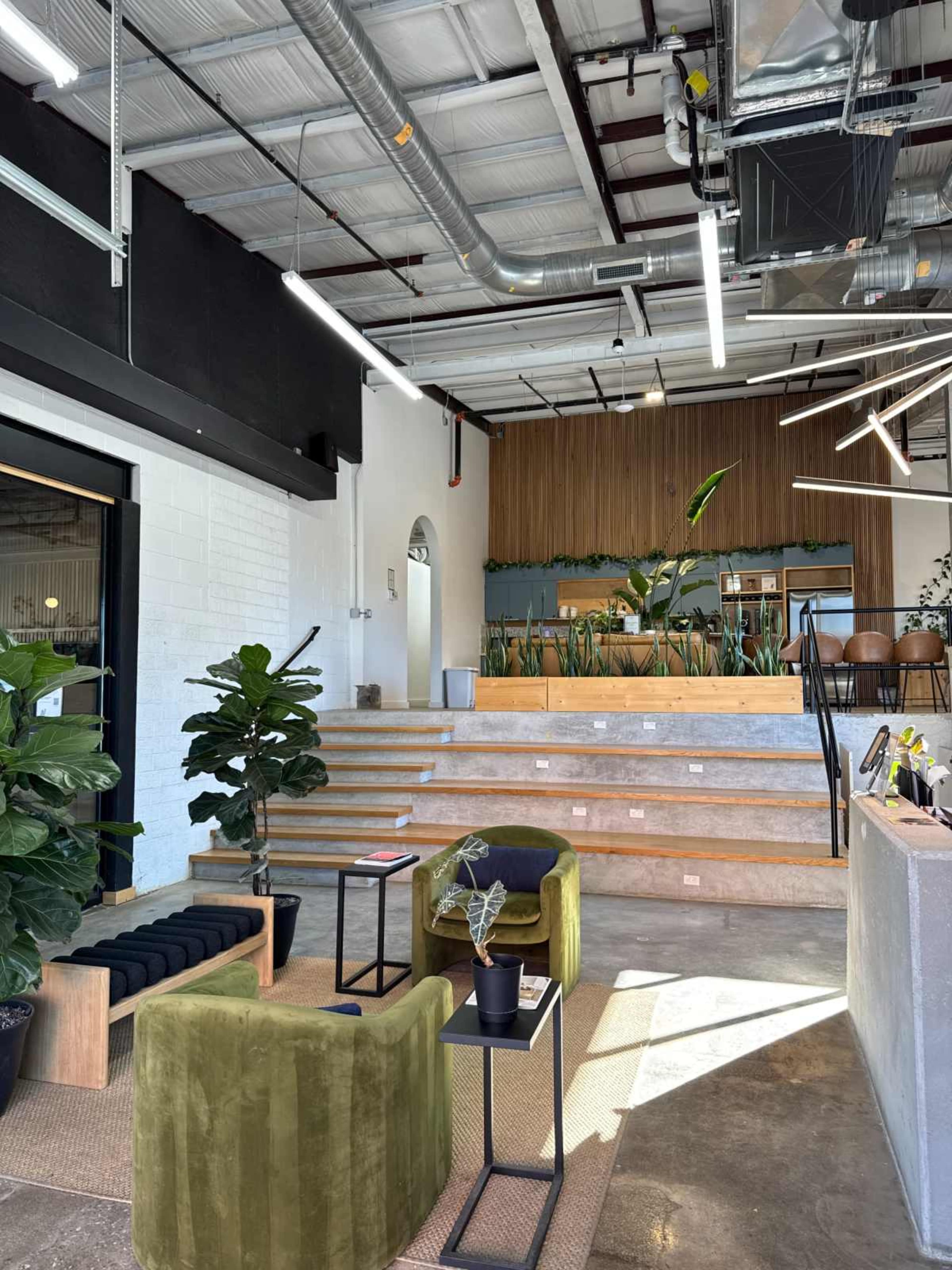 The image shows a modern interior space with a seating area featuring green and black furniture, a staircase leading to a higher level, and plants integrated into the decor.
