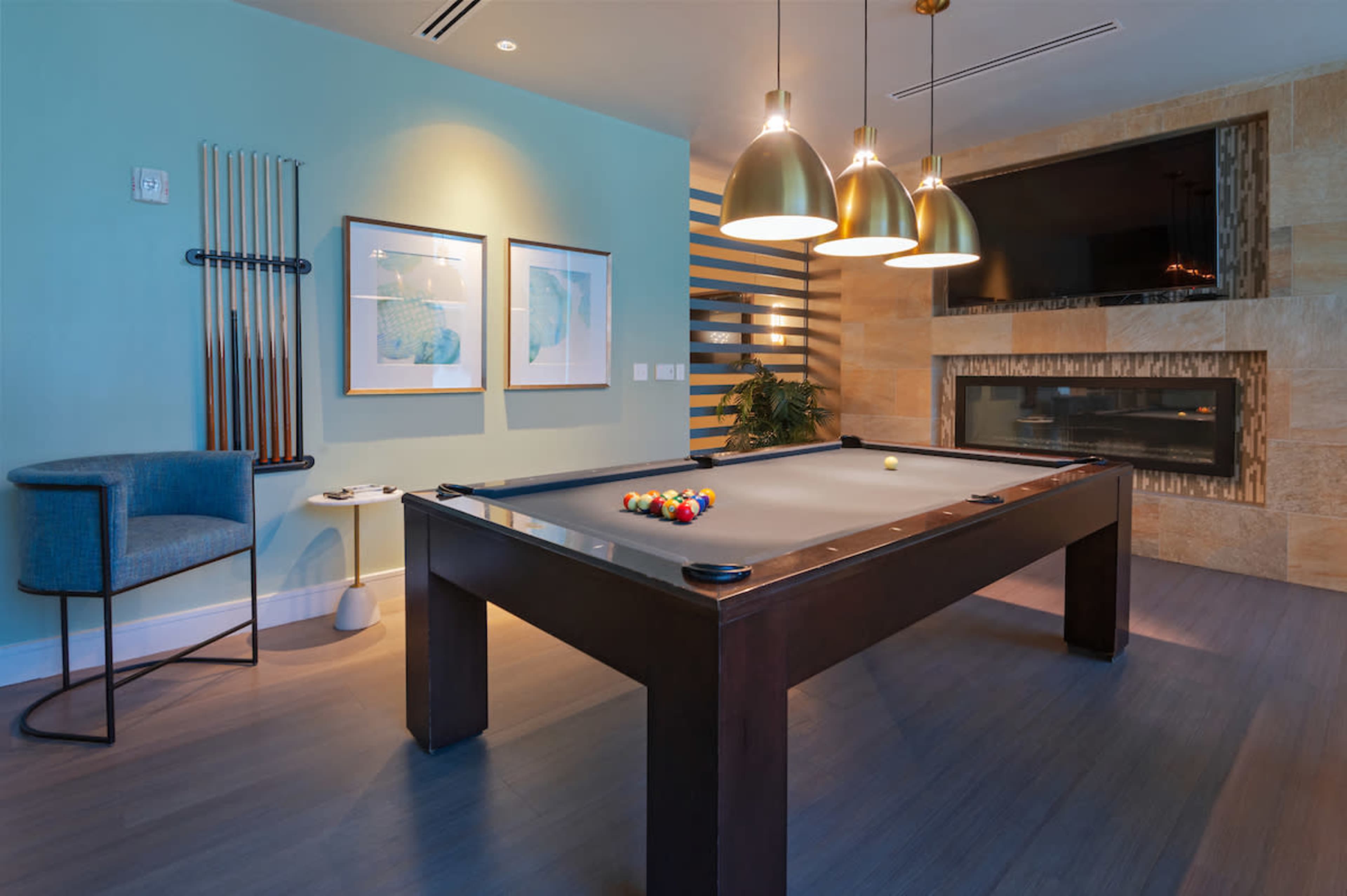 A pool table is centered in a modern game room with decorative walls, pendant lighting, and a fireplace.
