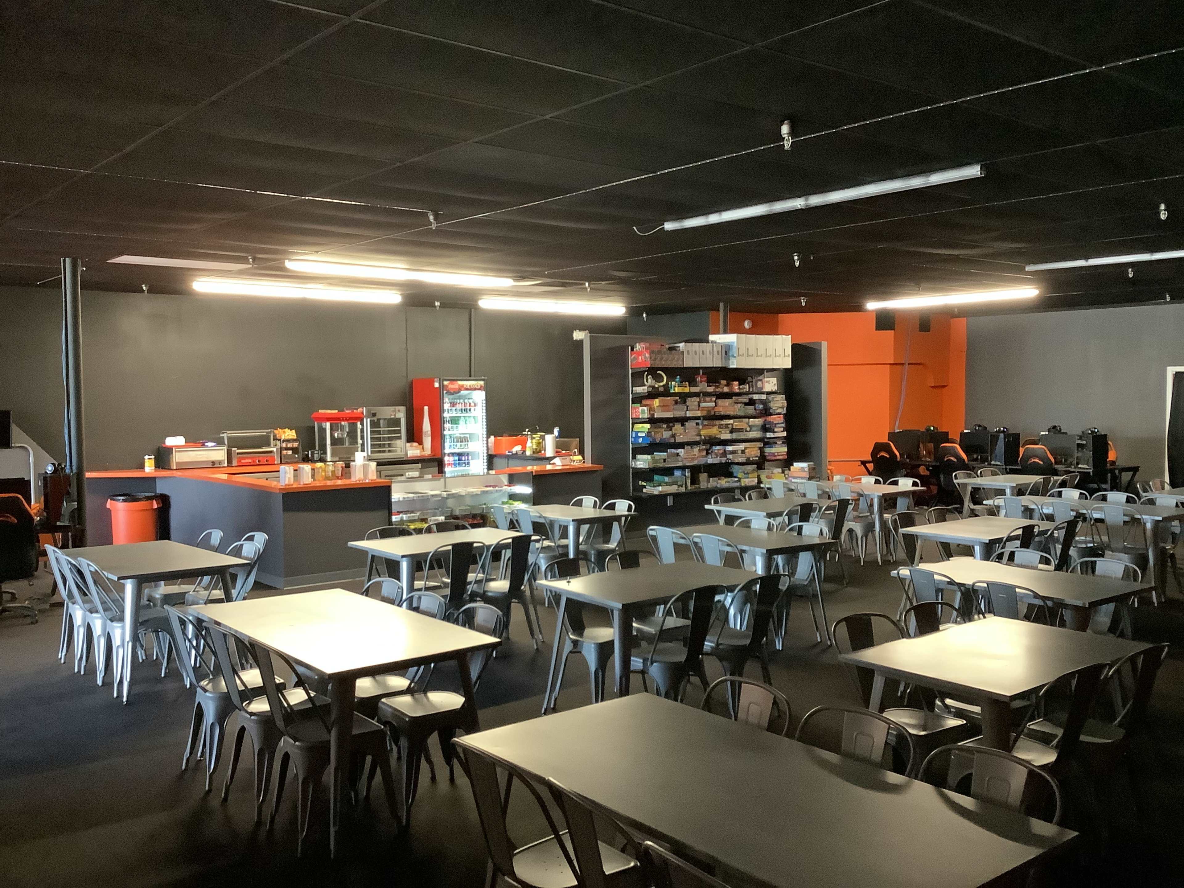 A spacious dining area features multiple metal tables and chairs, with a snack bar and display shelves along one wall.