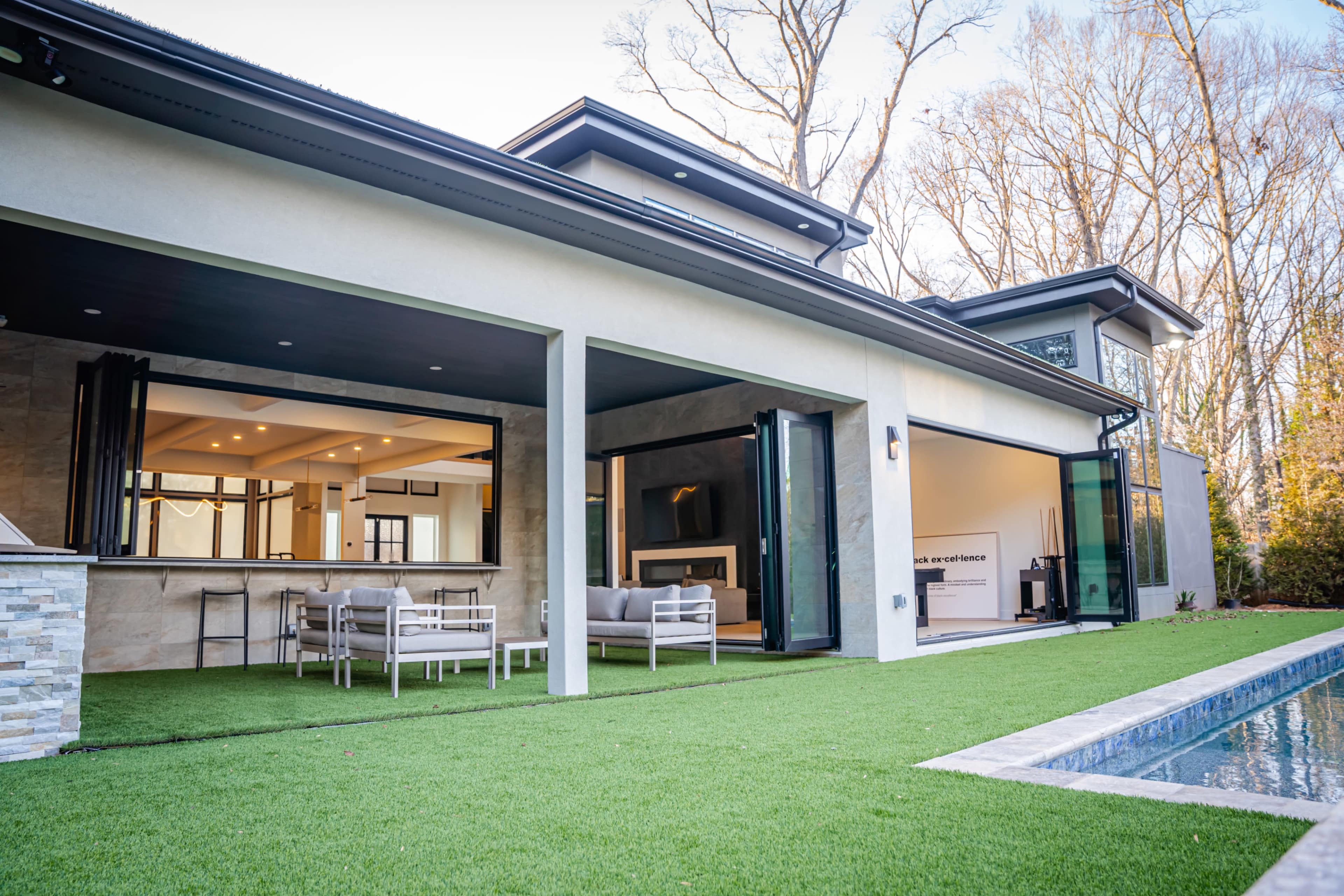The image shows a modern house with large glass doors opening to a patio and a well-maintained lawn, adjacent to a swimming pool.