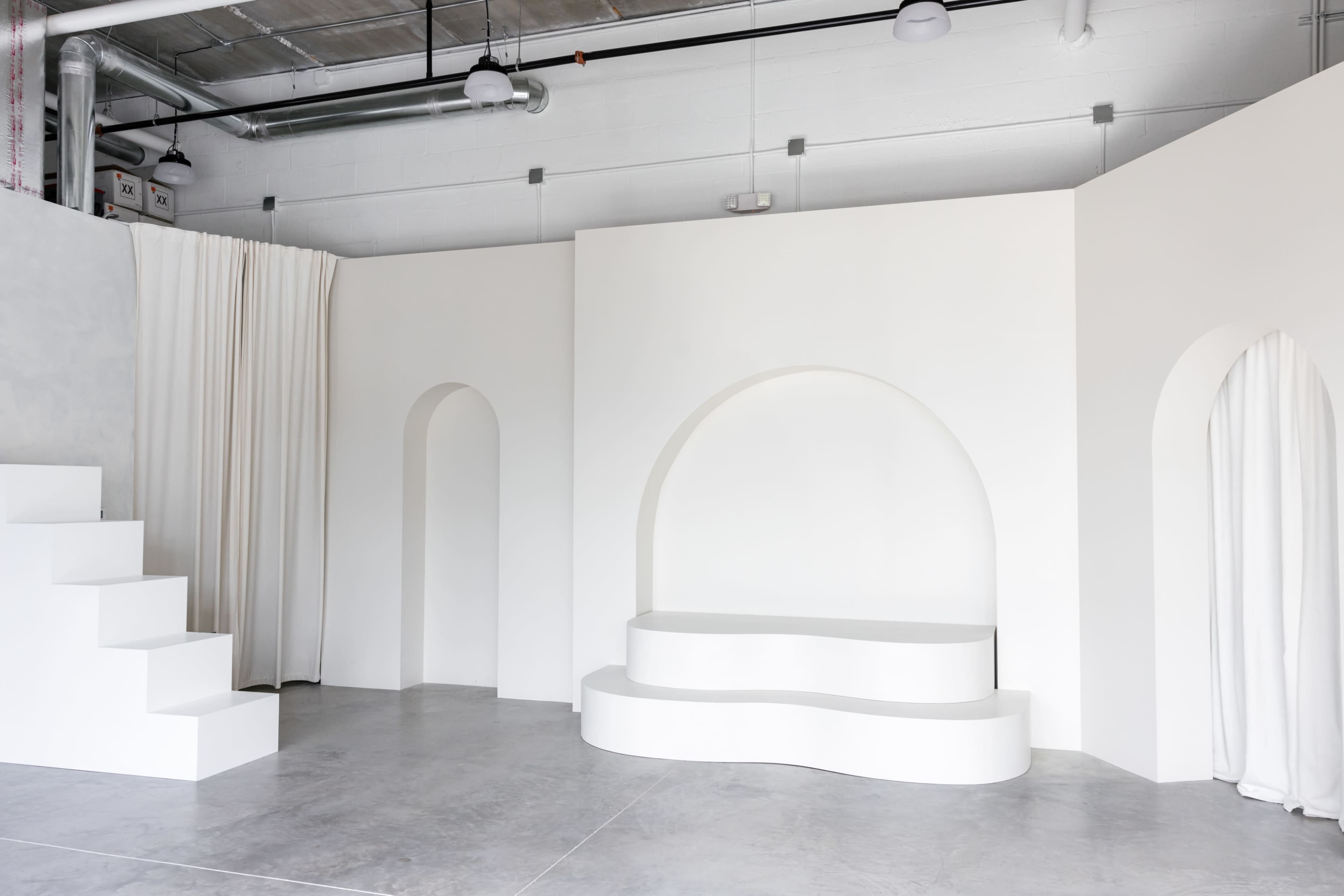 A minimalist interior space featuring white walls, steps leading to an archway, and a curved seating area.