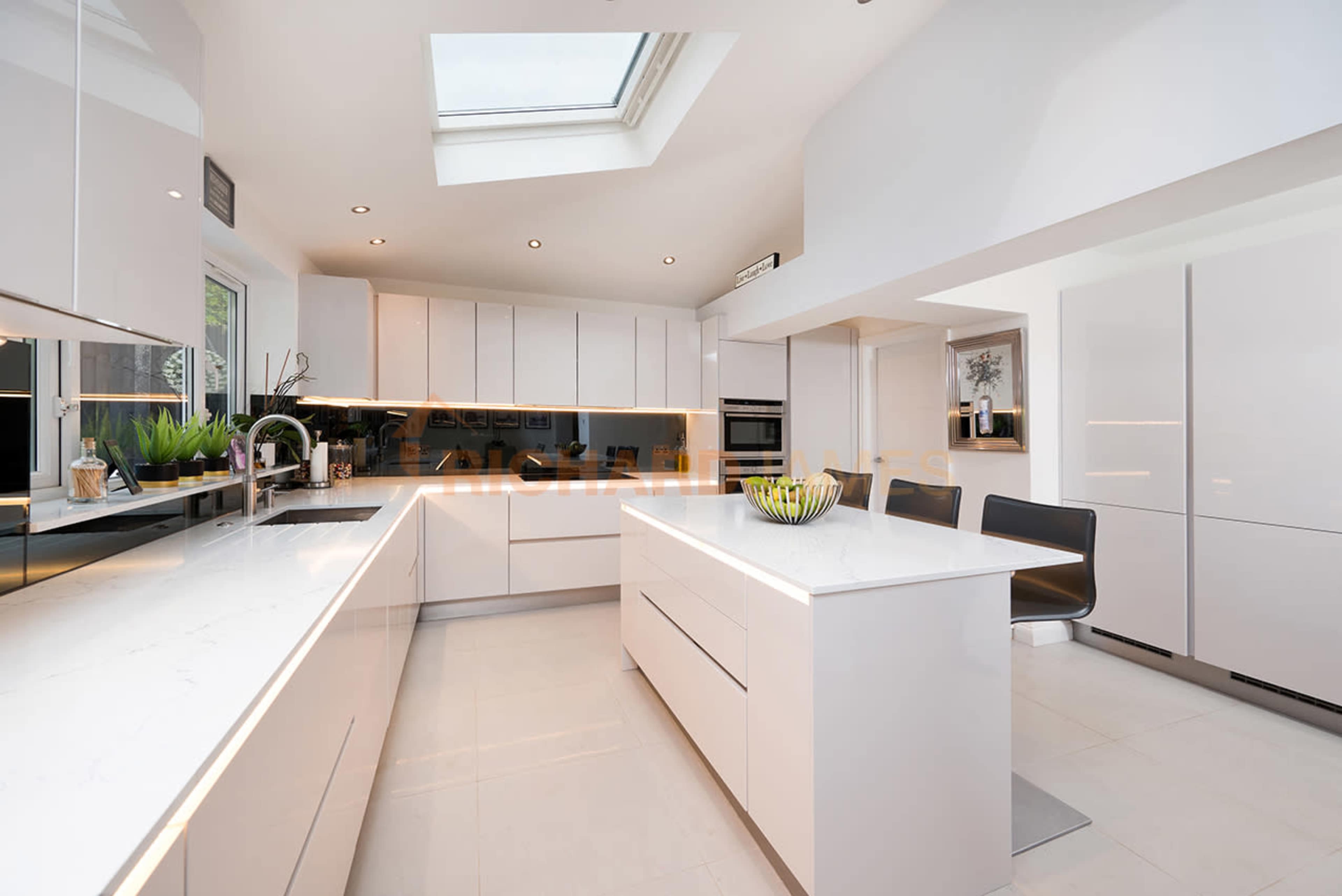 A modern kitchen with white cabinetry, a central island, and large skylights illuminating the space.