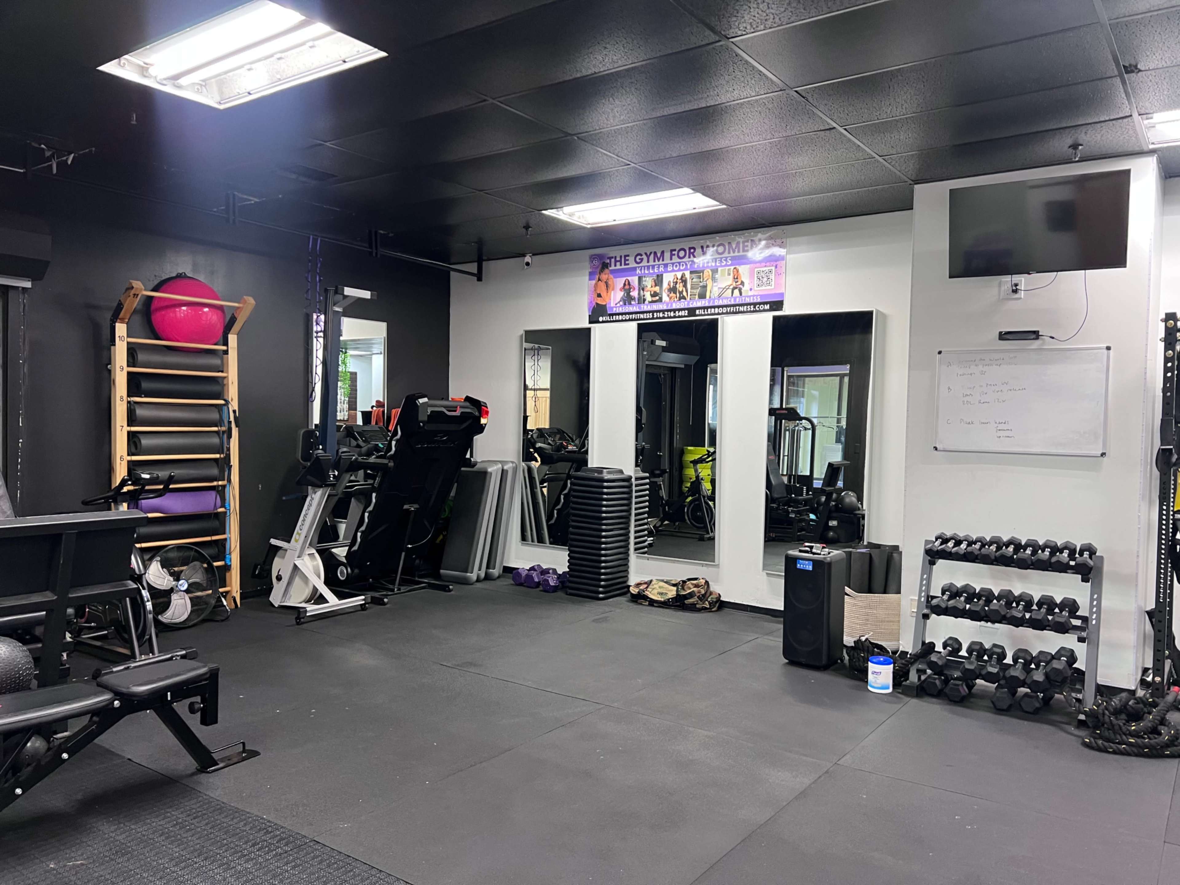 A gym interior featuring exercise equipment, weights, and a wall-mounted television.