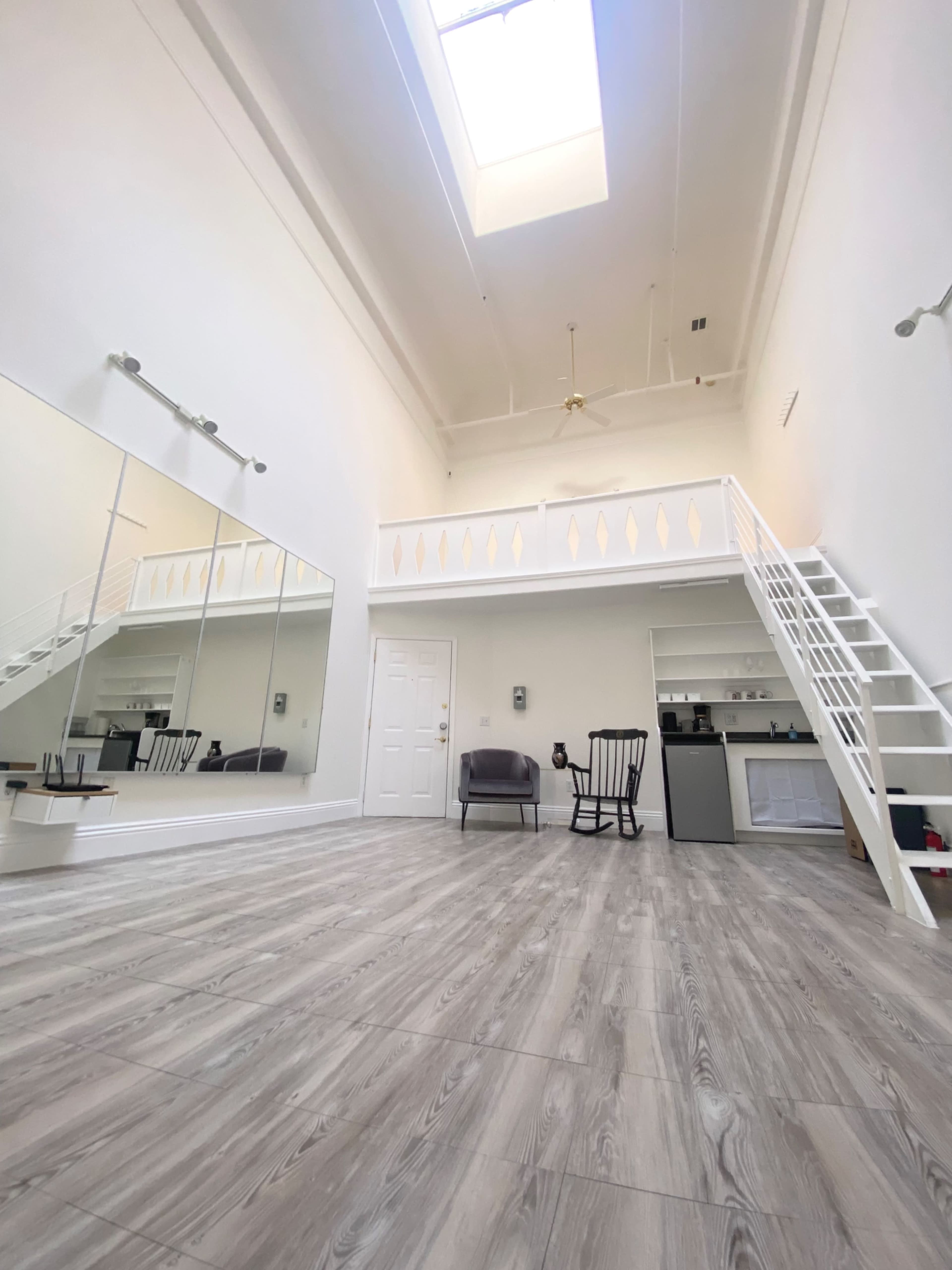 A spacious room with high ceilings, featuring a skylight, a mirror wall, and a small loft area with a staircase.