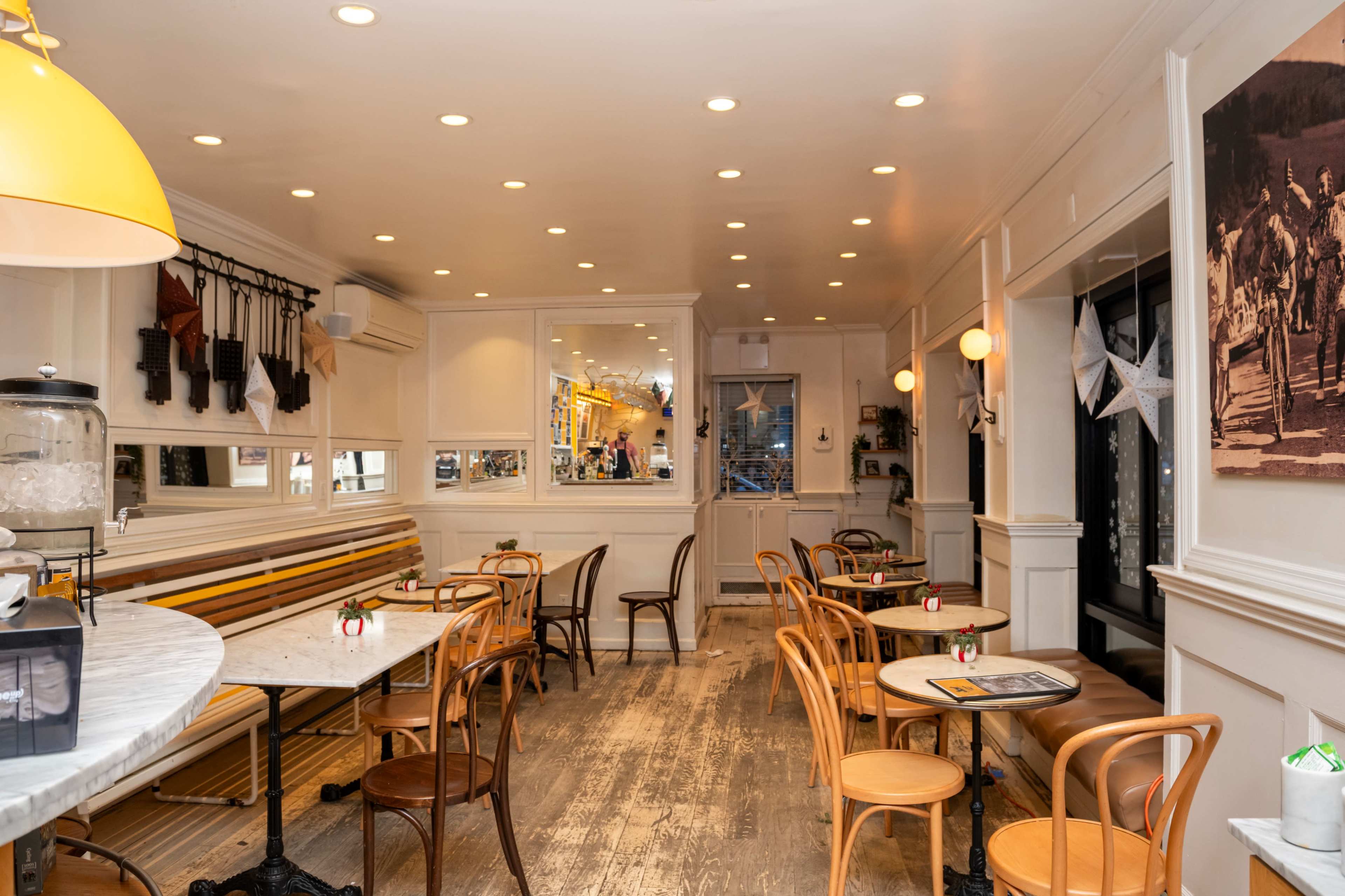 The image shows a cozy café interior with wooden furniture, multiple tables, and warm lighting.