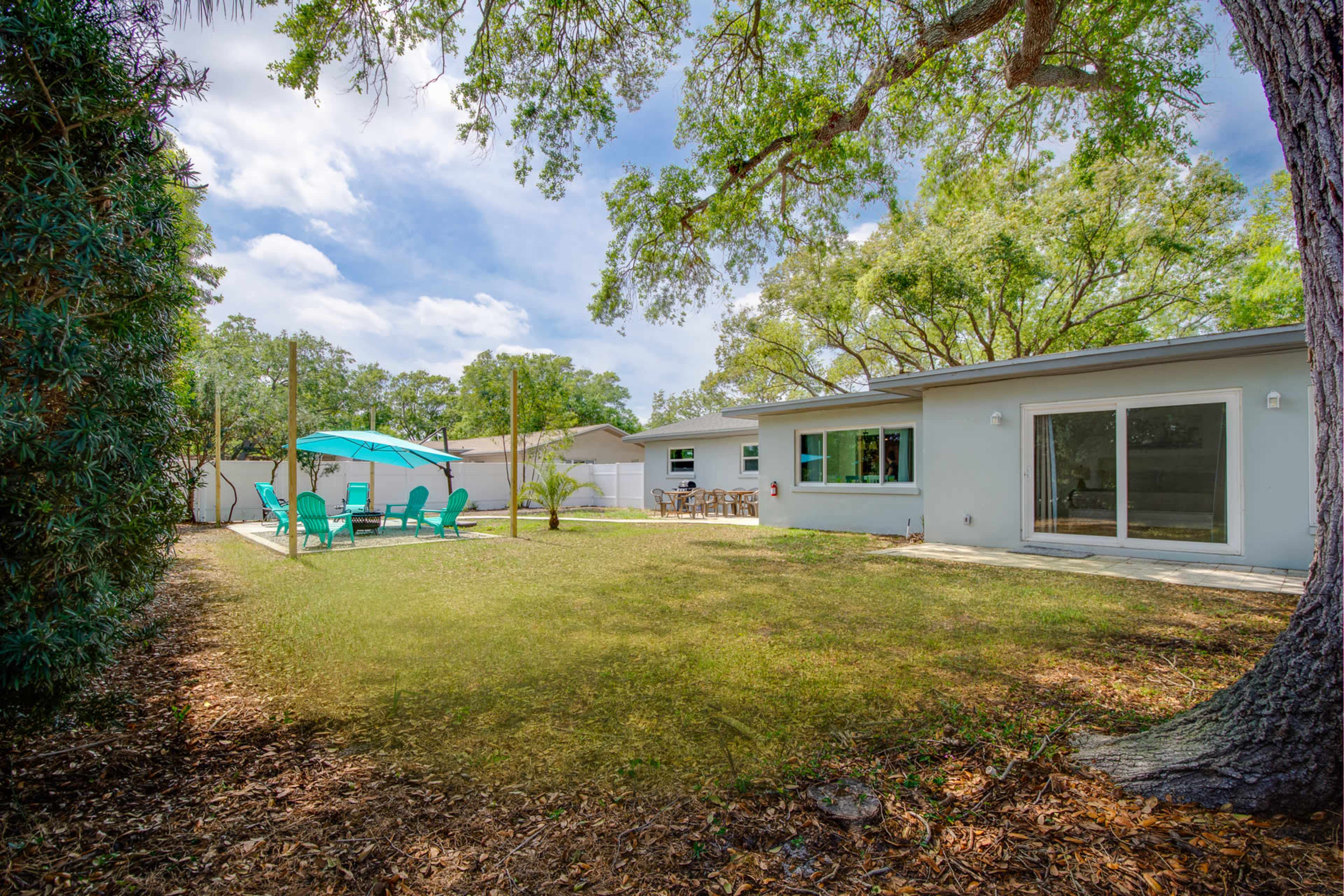 A spacious backyard with a green lawn, a patio area with chairs, and trees providing shade.