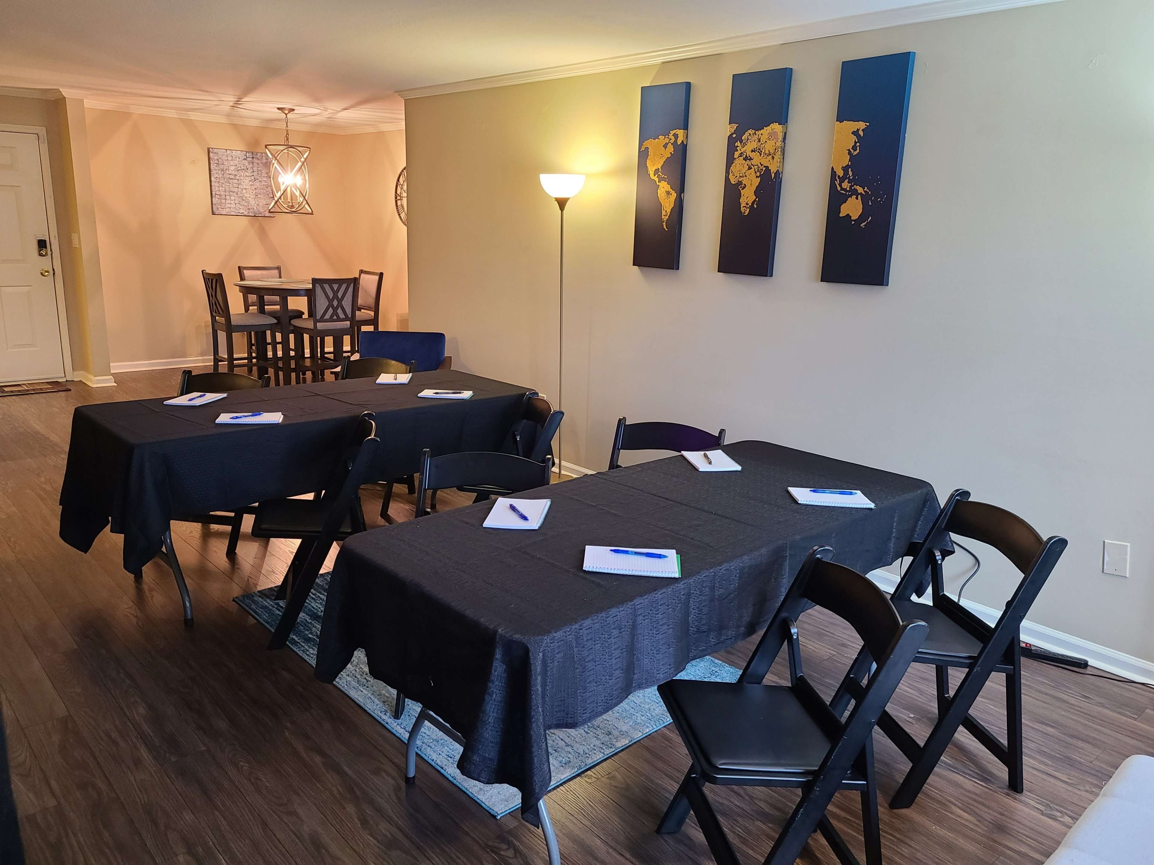 A meeting space with several black tables and chairs arranged neatly, featuring a light source and framed world maps on the wall.