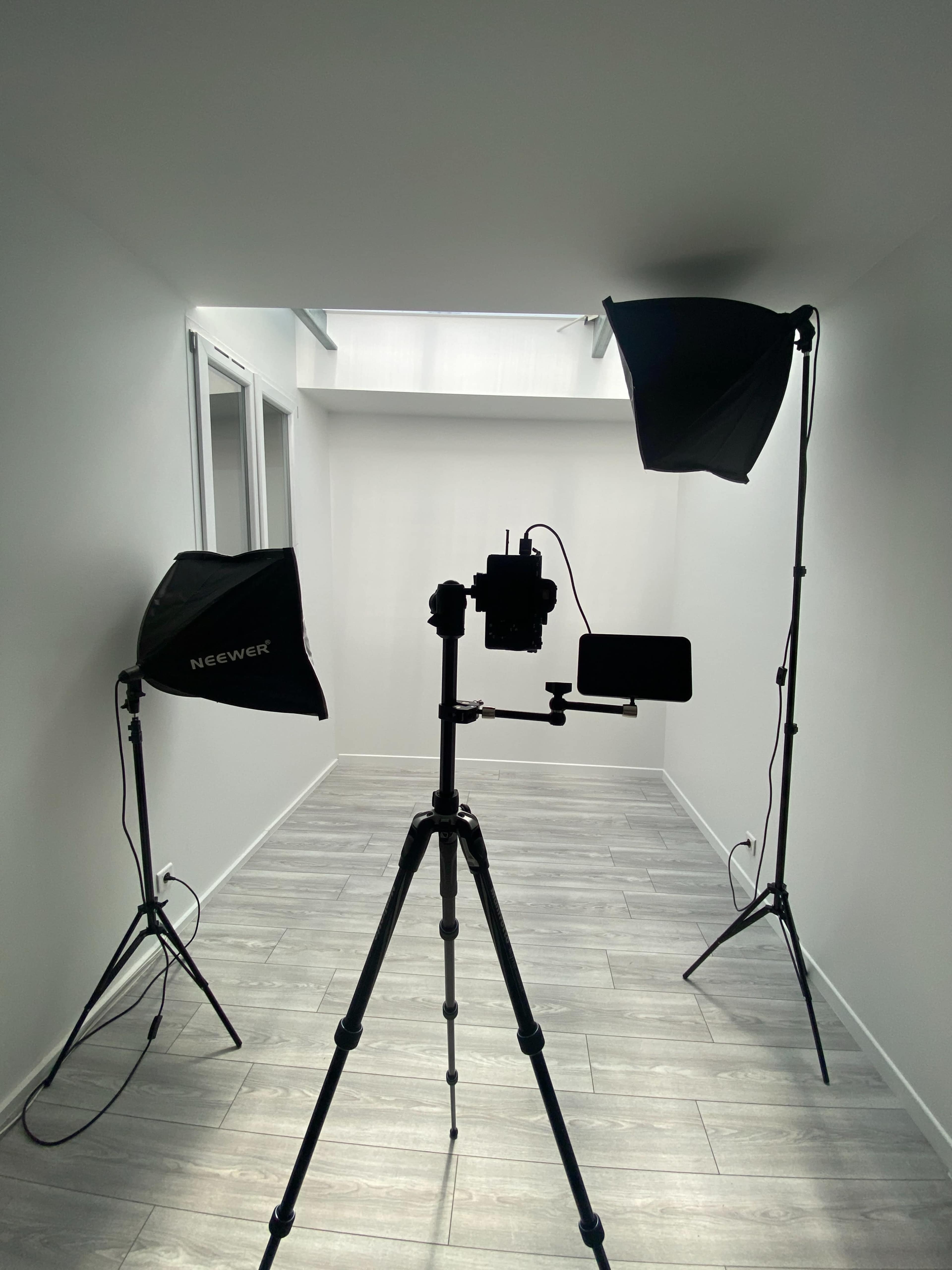 A photography setup is positioned in a minimalistic room with two softbox lights and a camera mounted on a tripod.