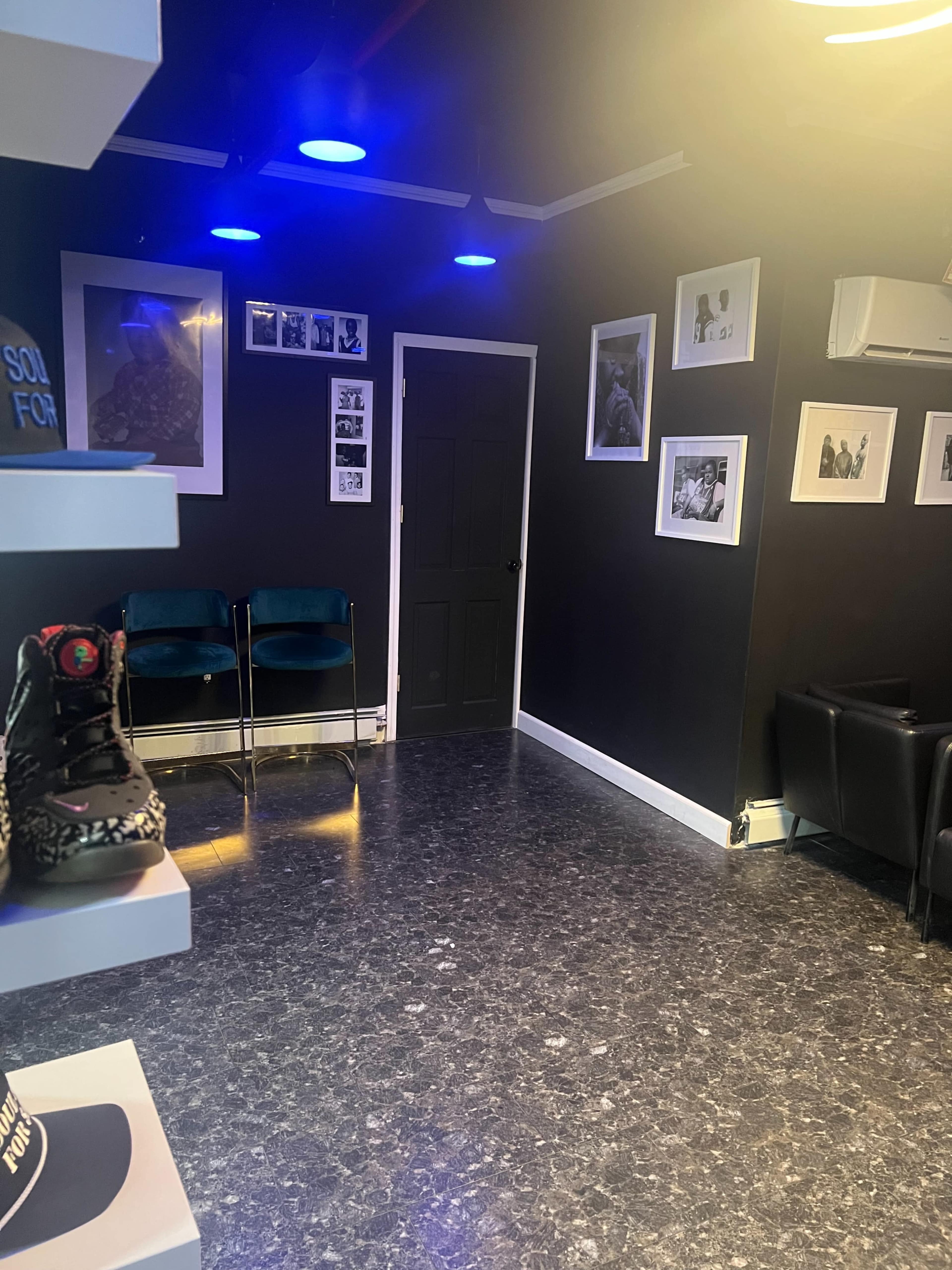 A sleek, modern interior of a room featuring black walls, framed photographs, two blue chairs, and a door.