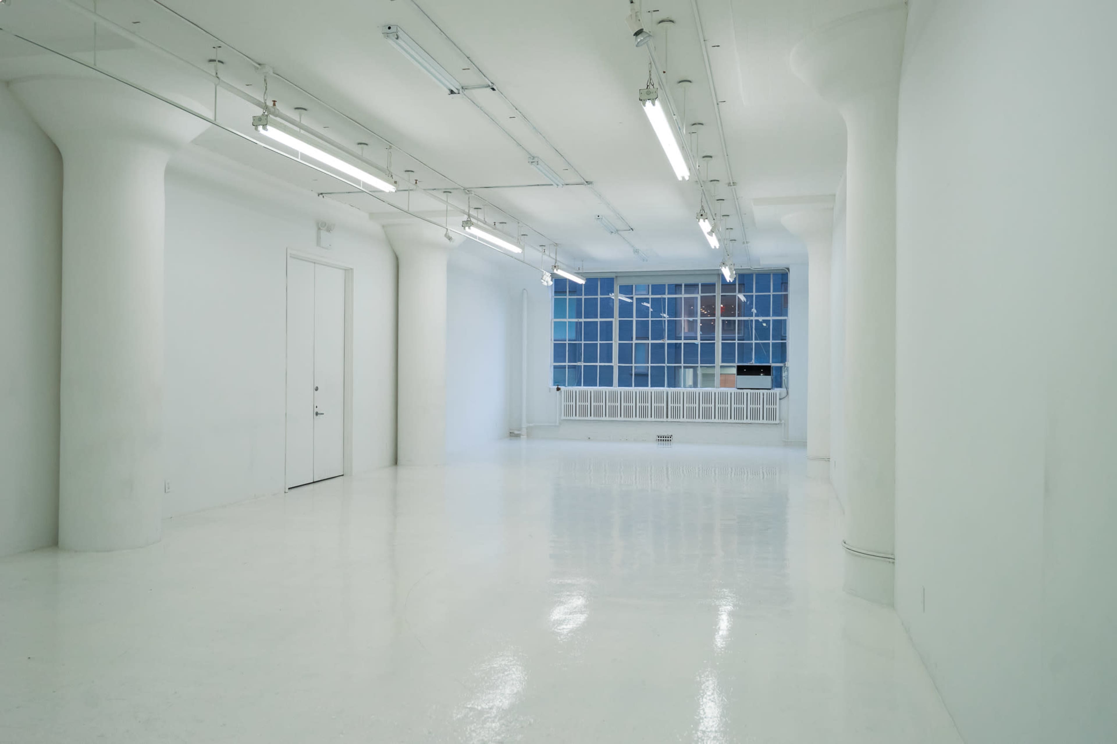 A spacious, empty room with white walls, polished floors, and large windows letting in natural light.