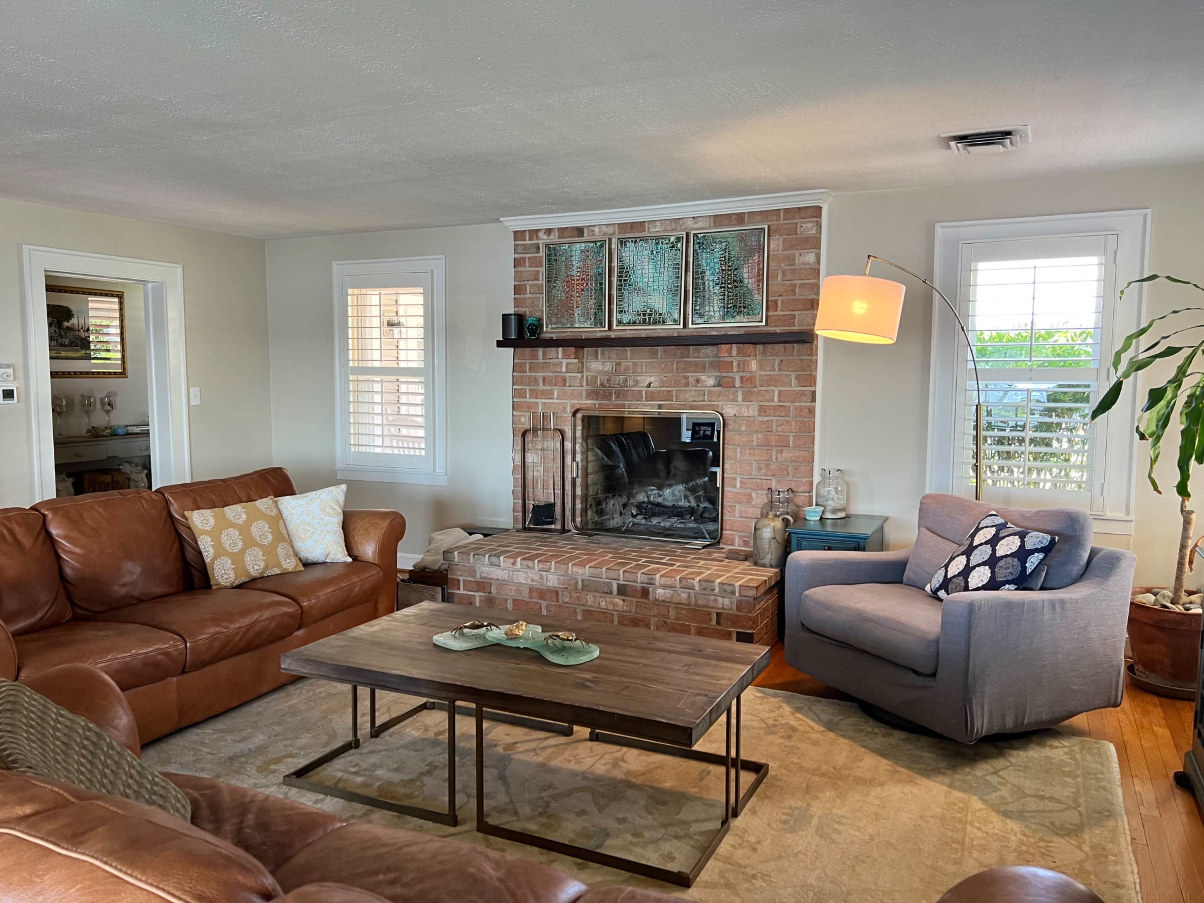 The living room features a brick fireplace, a leather sofa, an armchair, and a coffee table with decorative items.