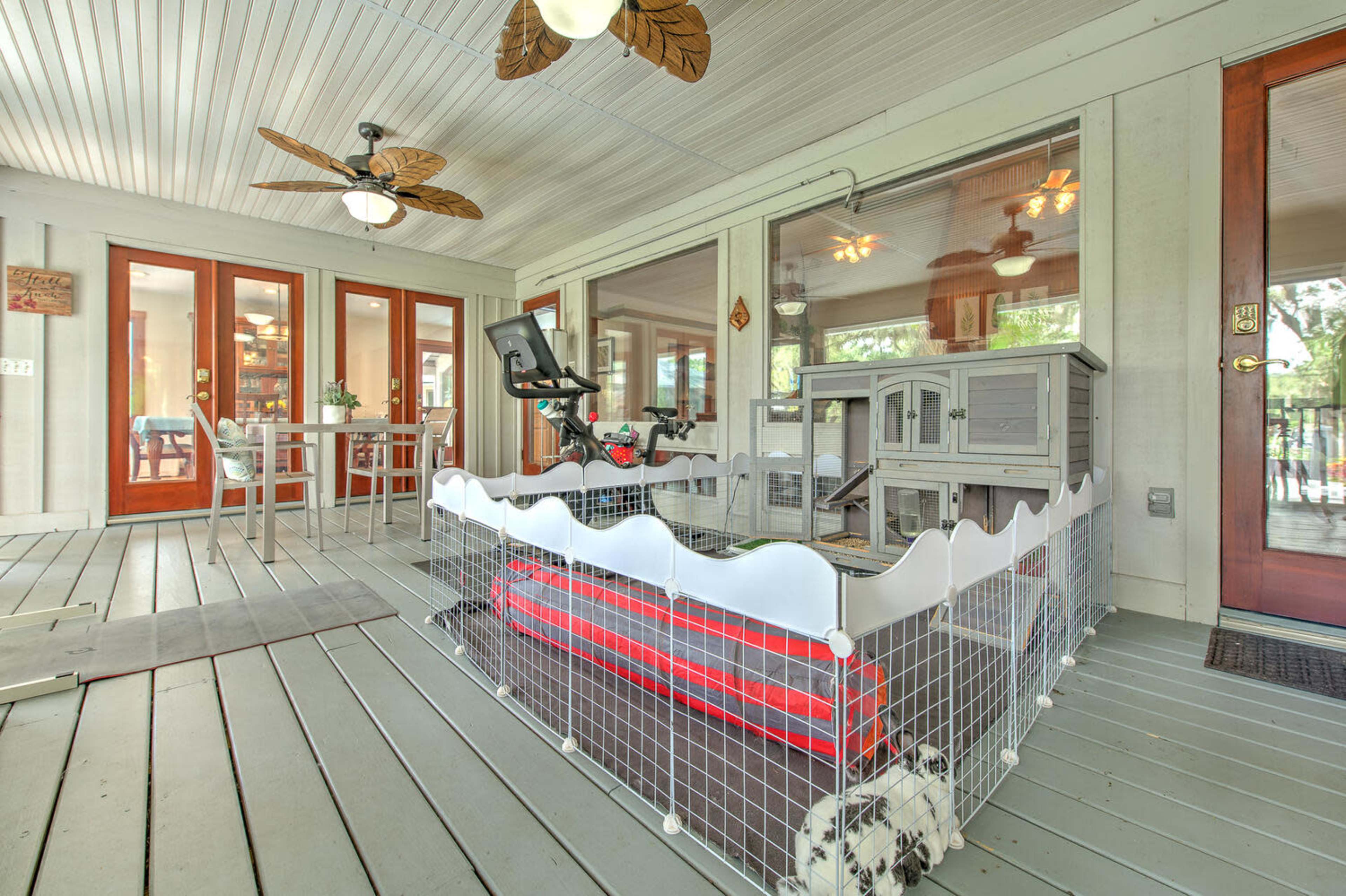 A playpen for a pet is set up on a covered porch with a dining table and chairs in the background.
