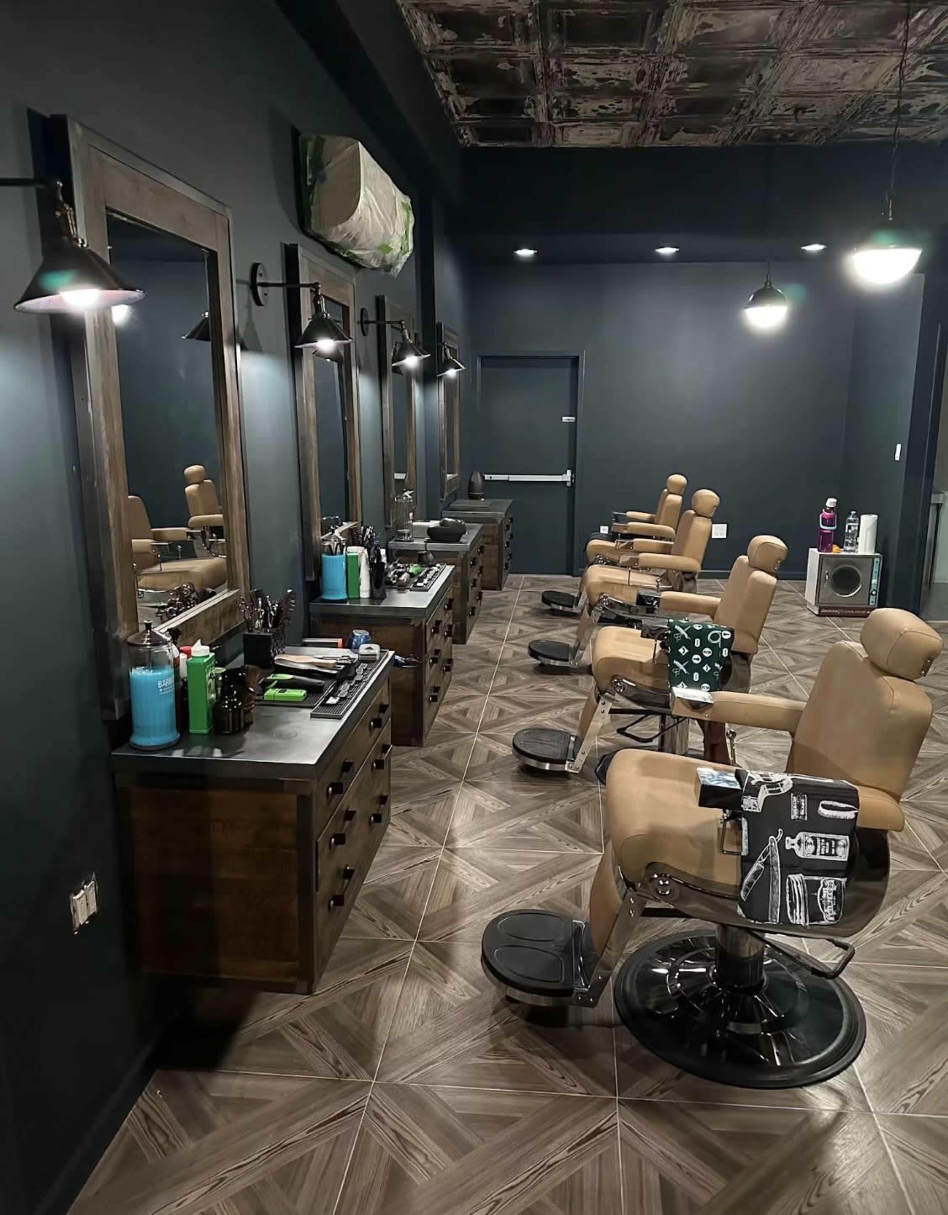 The image shows a modern barbershop with several styling chairs, mirrors, and tools organized along dark walls and patterned flooring.