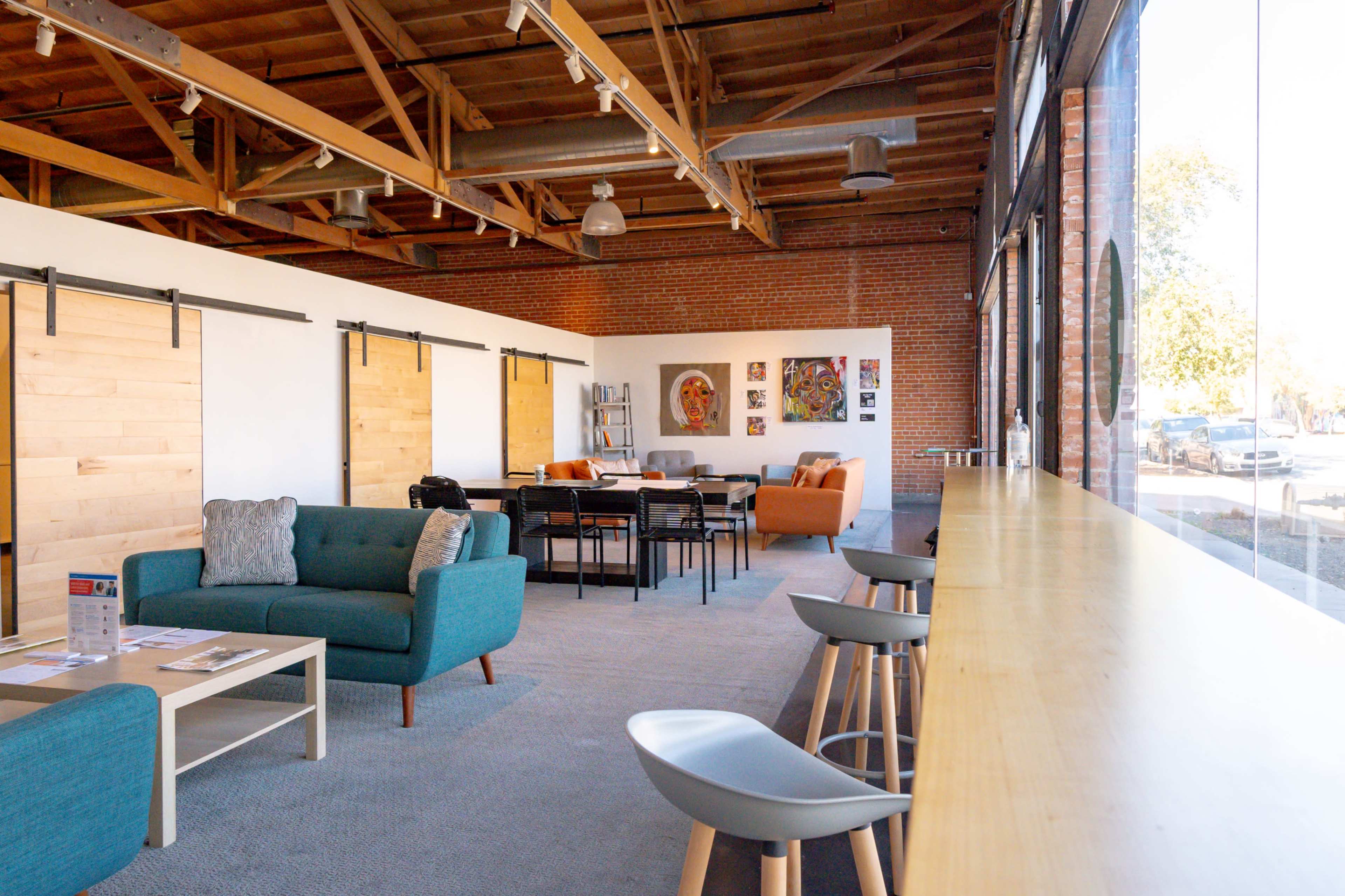 A spacious interior of a modern community space with wooden beams, seating areas, and artwork on the walls.
