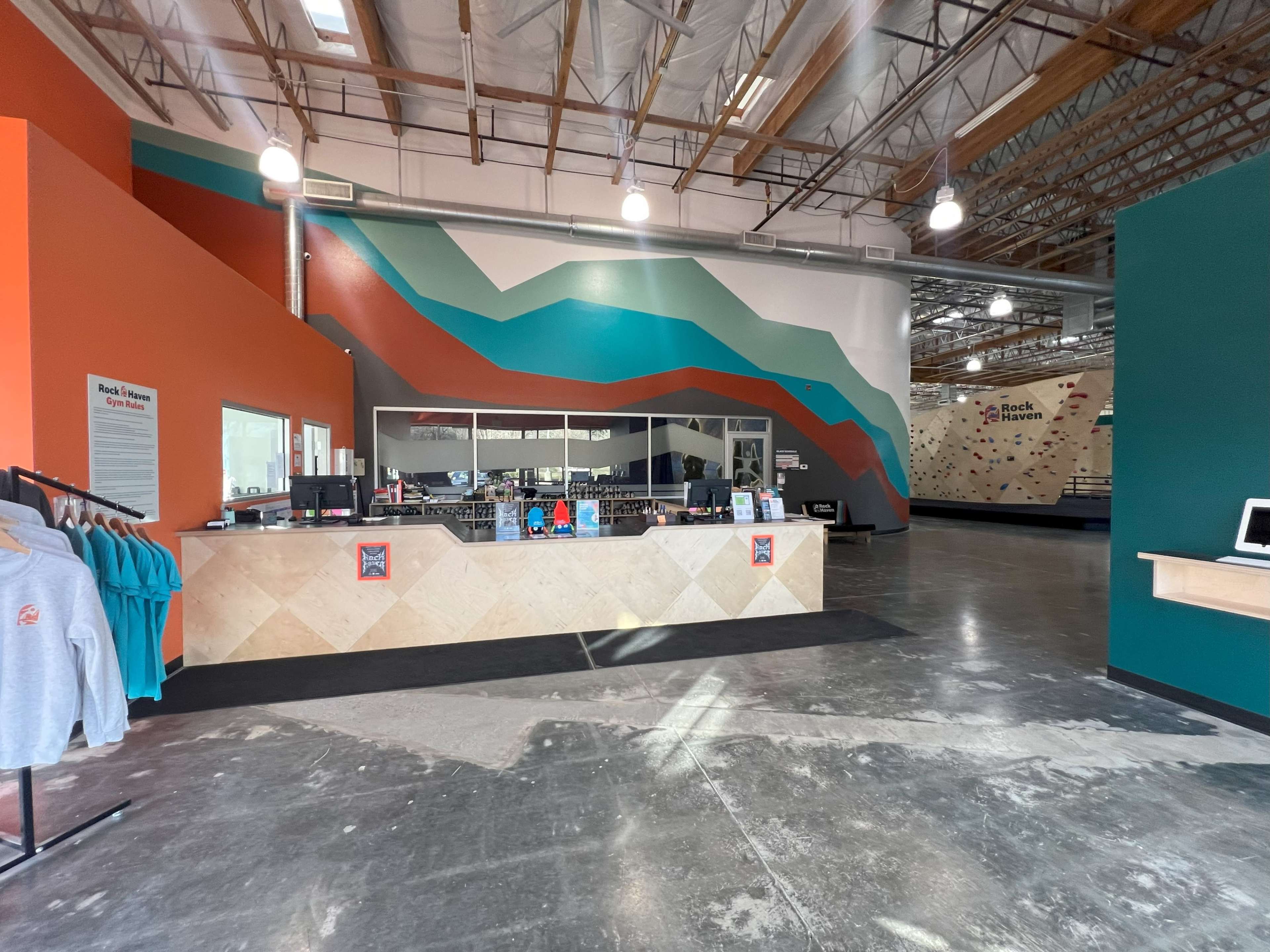 A brightly colored indoor climbing gym with a reception area featuring a geometric wall design and climbing walls in the background.