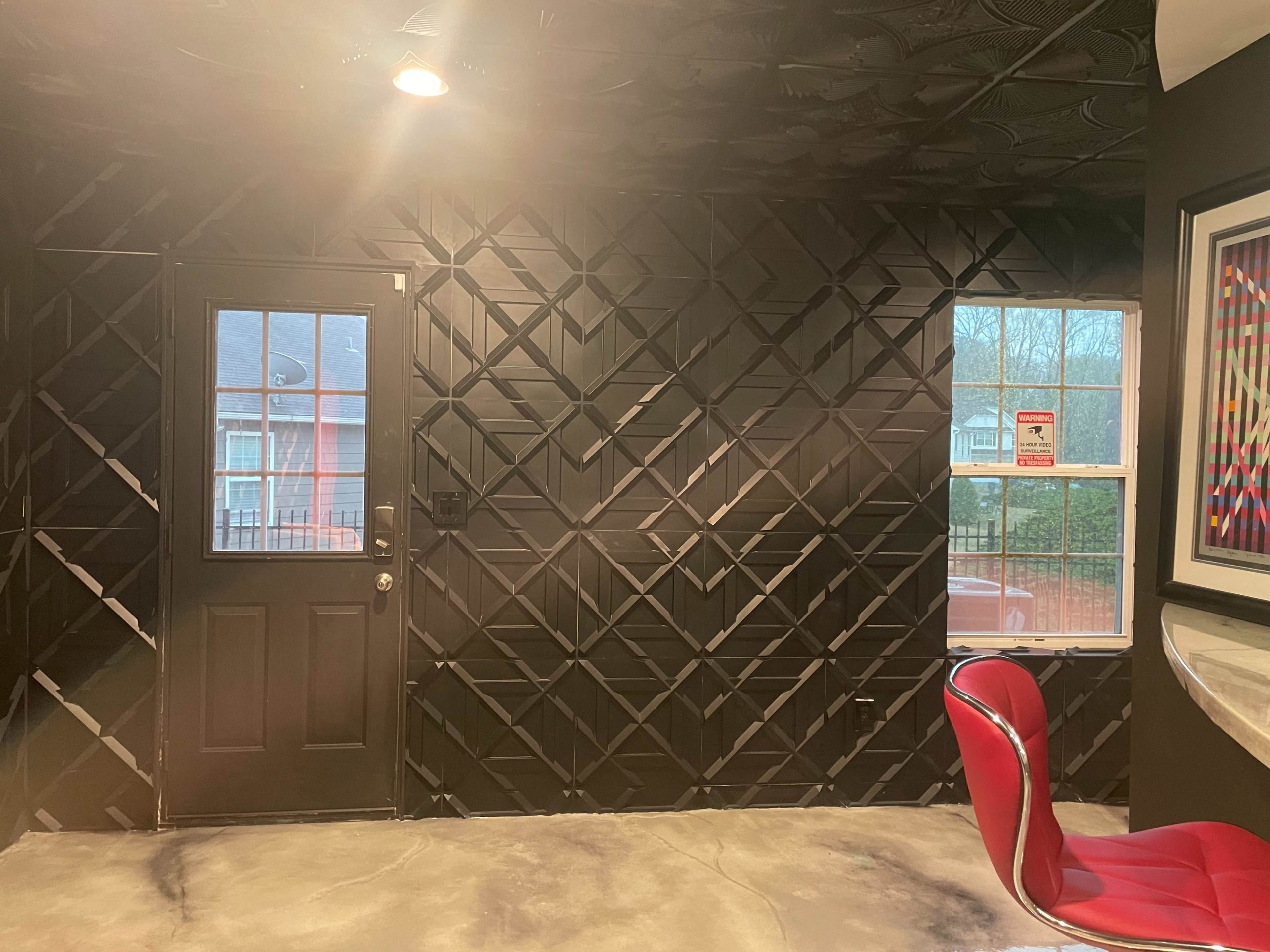The image shows a room with black patterned walls, a door on the left, a window on the right, and a red chair positioned near a counter.