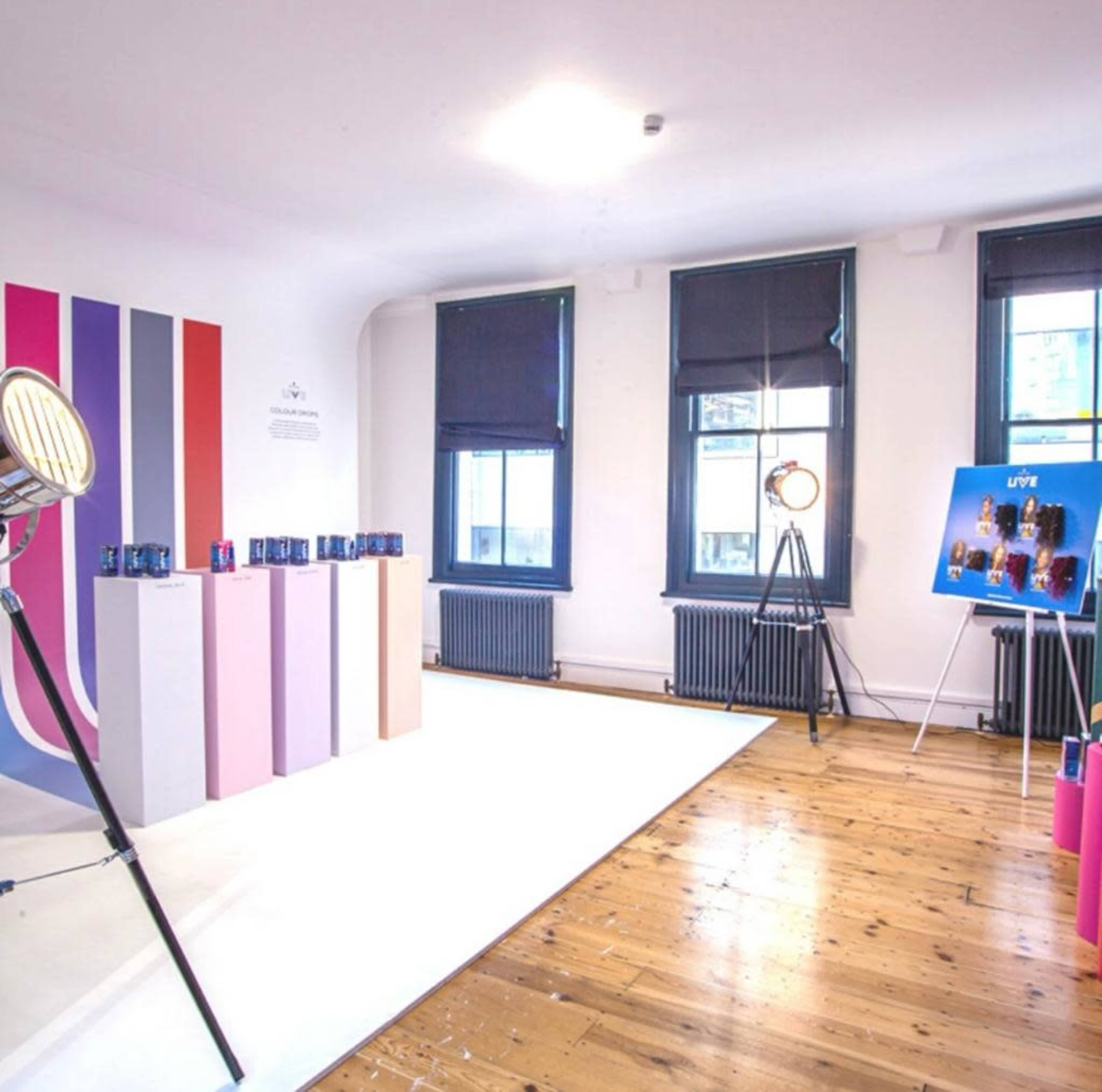 A bright room with a white floor, featuring colored striped walls, display pedestals for products, and a photo on an easel.