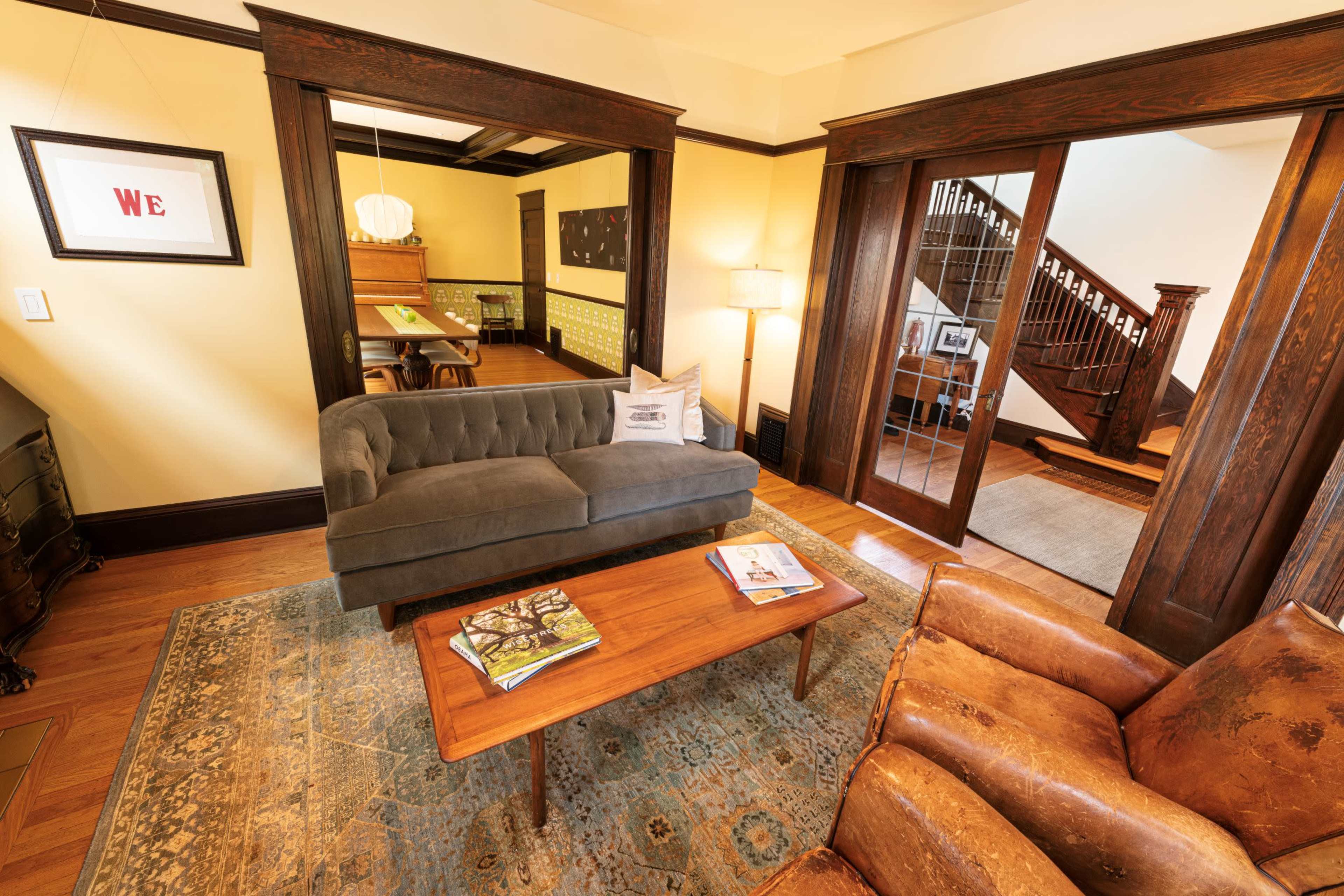 A cozy living room with a gray sofa, a wooden coffee table, and a view of an adjacent room with a staircase and desk.