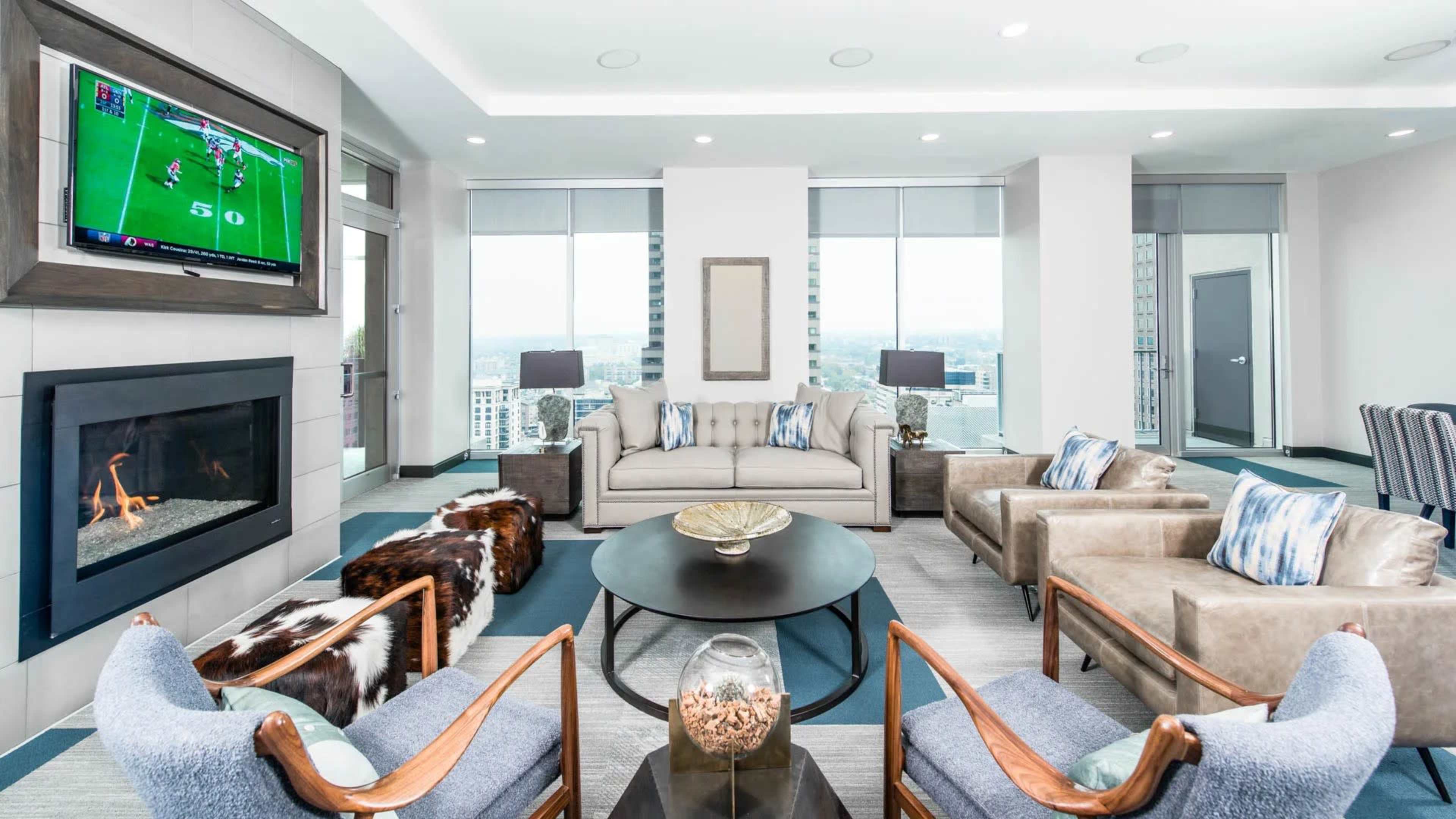 A modern living room features a television mounted on the wall, a fireplace, and seating arranged around a circular coffee table.