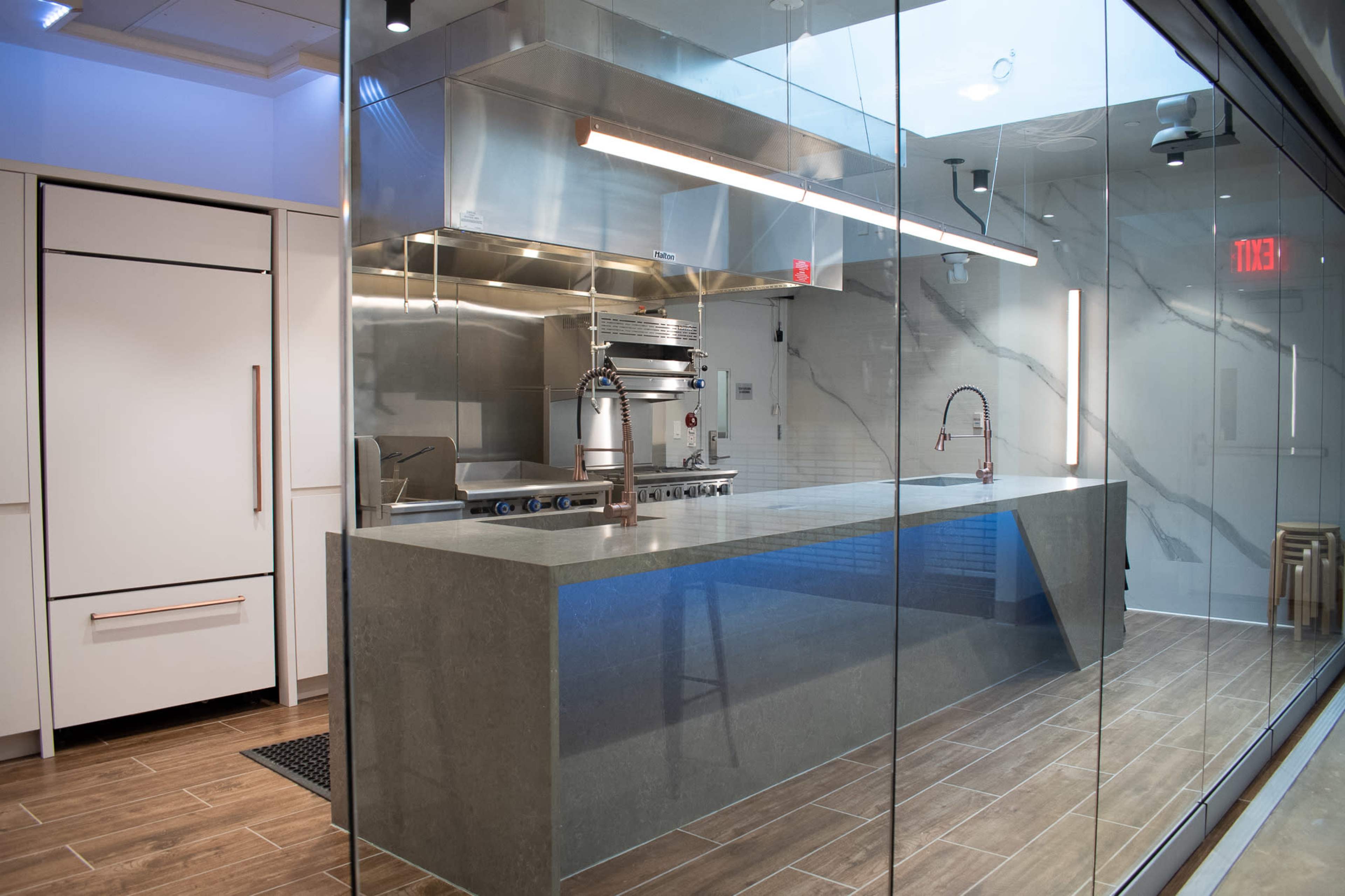 A modern kitchen with a stainless steel cooking area, a large stone countertop, and glass walls.