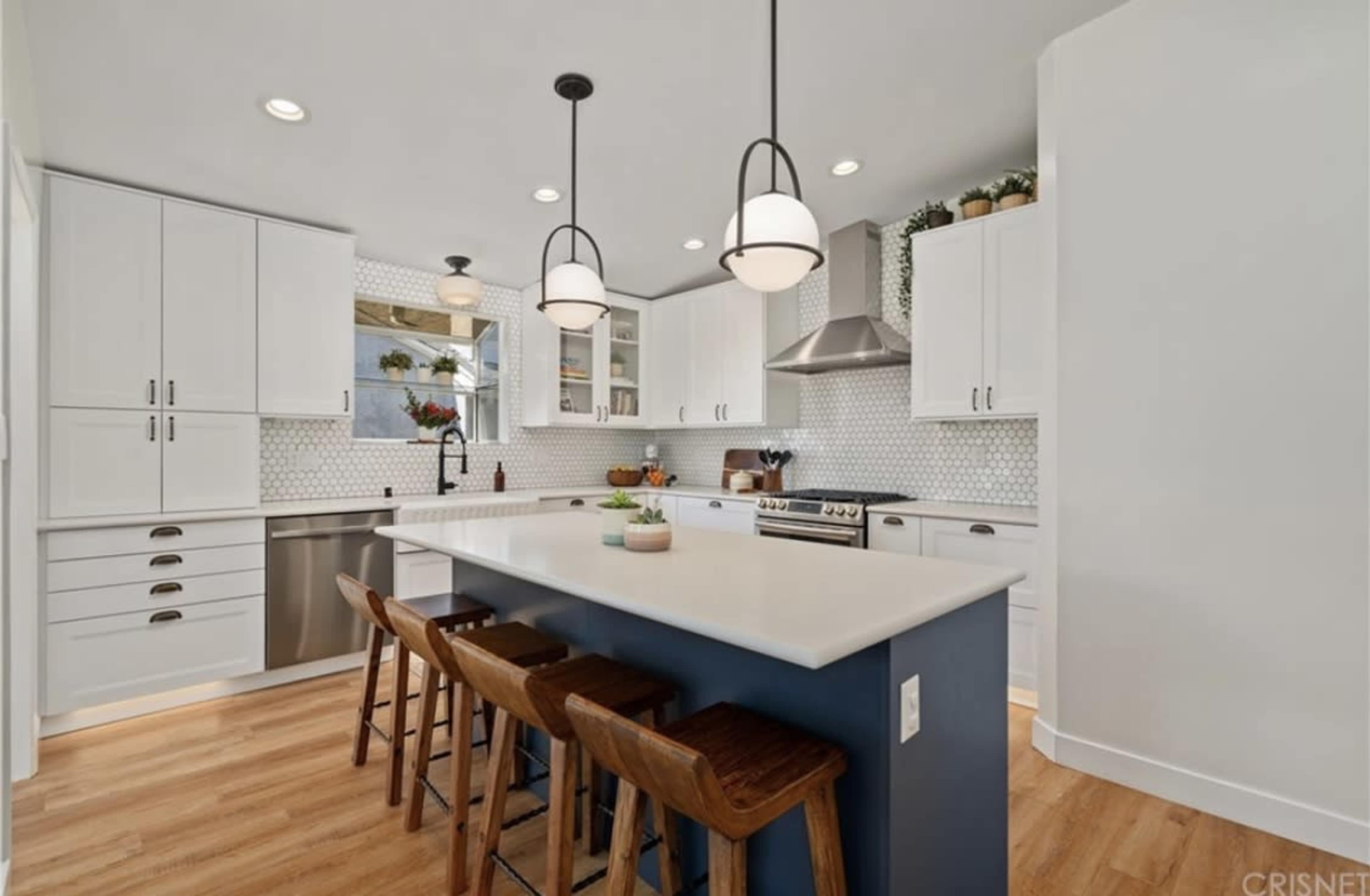 A modern kitchen features white cabinets, a large island with stools, and pendant lighting above the countertop.